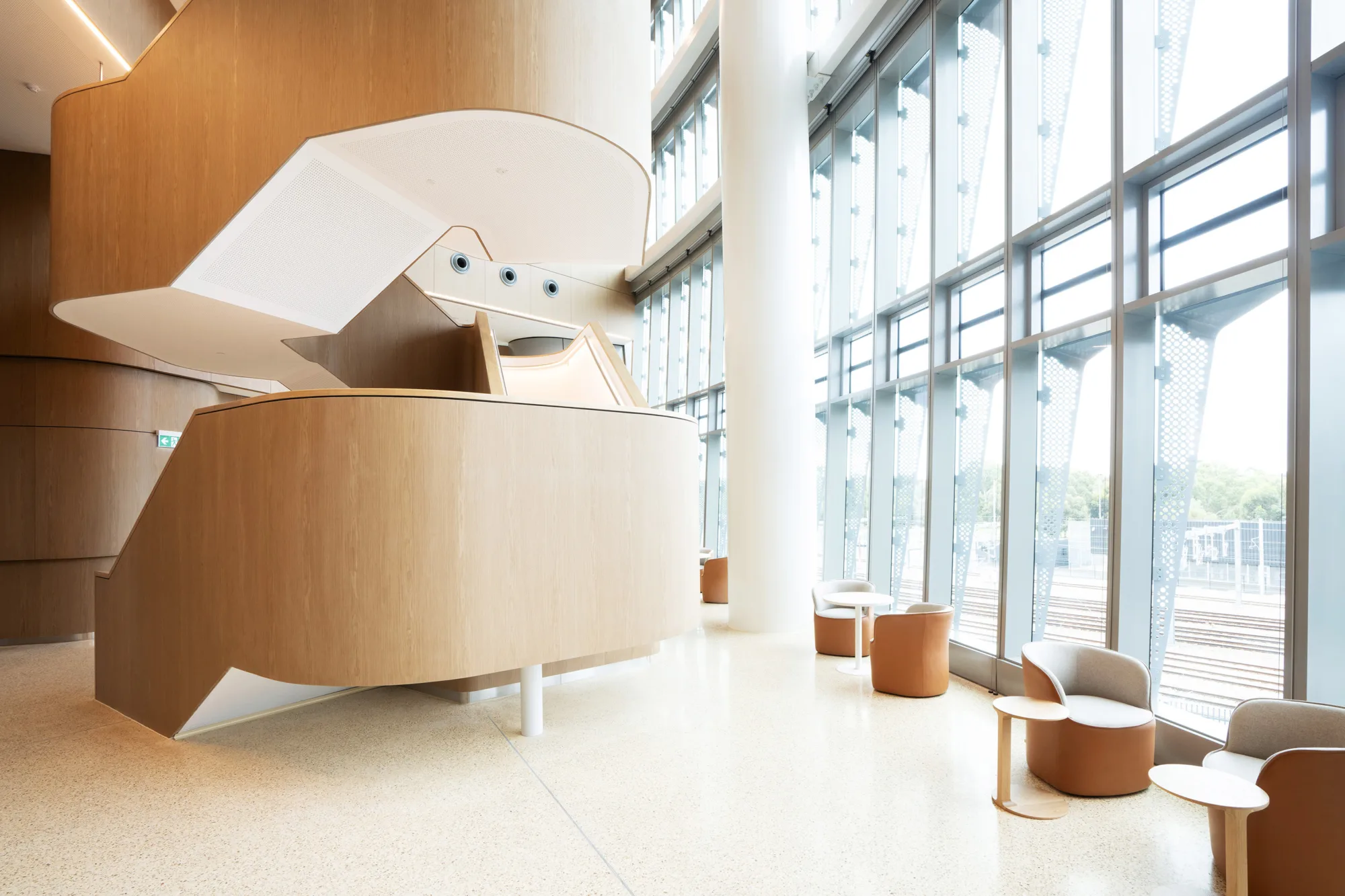 Interior view of a hospital lobby featuring wooden seating arranged neatly along the walls and a central wooden staircase.