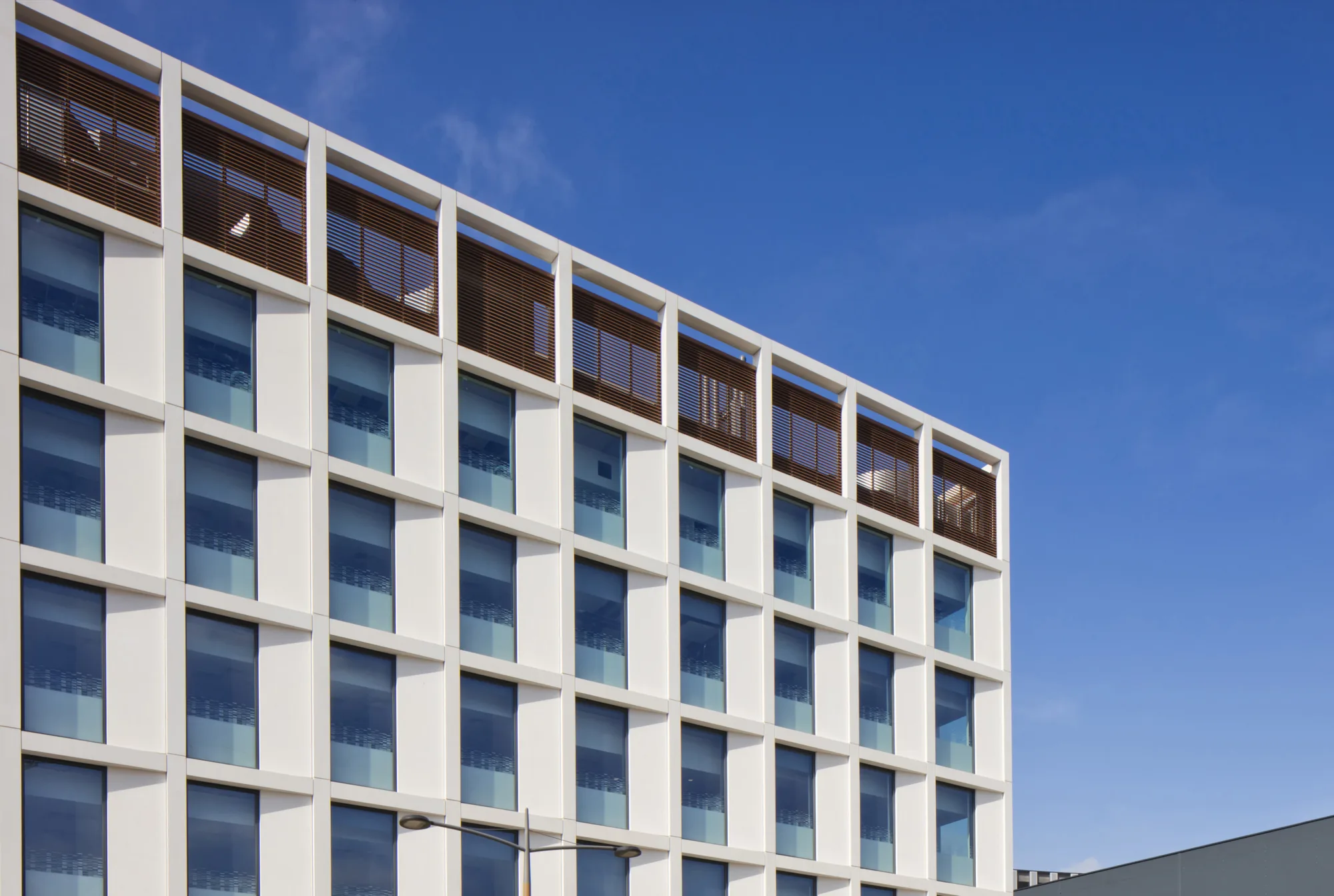 Upwards angled shot of a white walled building with regular square windows, against a blue sky