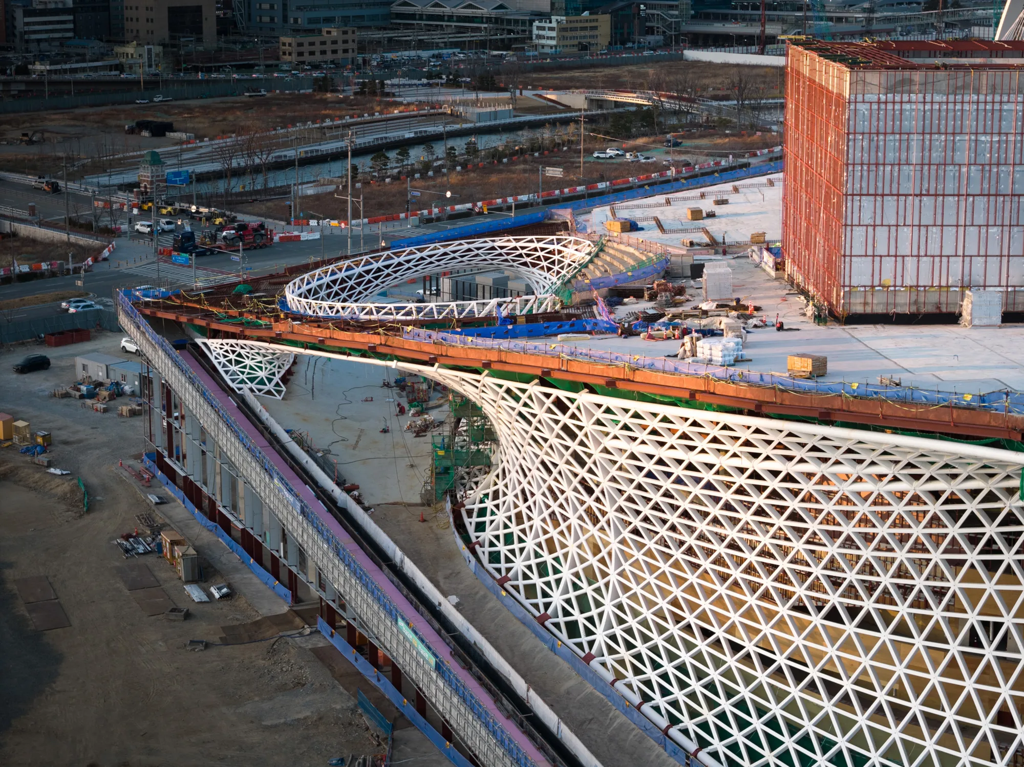 Aerial view of the Busan Opera House under construction, highlighting the transition between the signature twisted façade, the roof, and the public foyer.