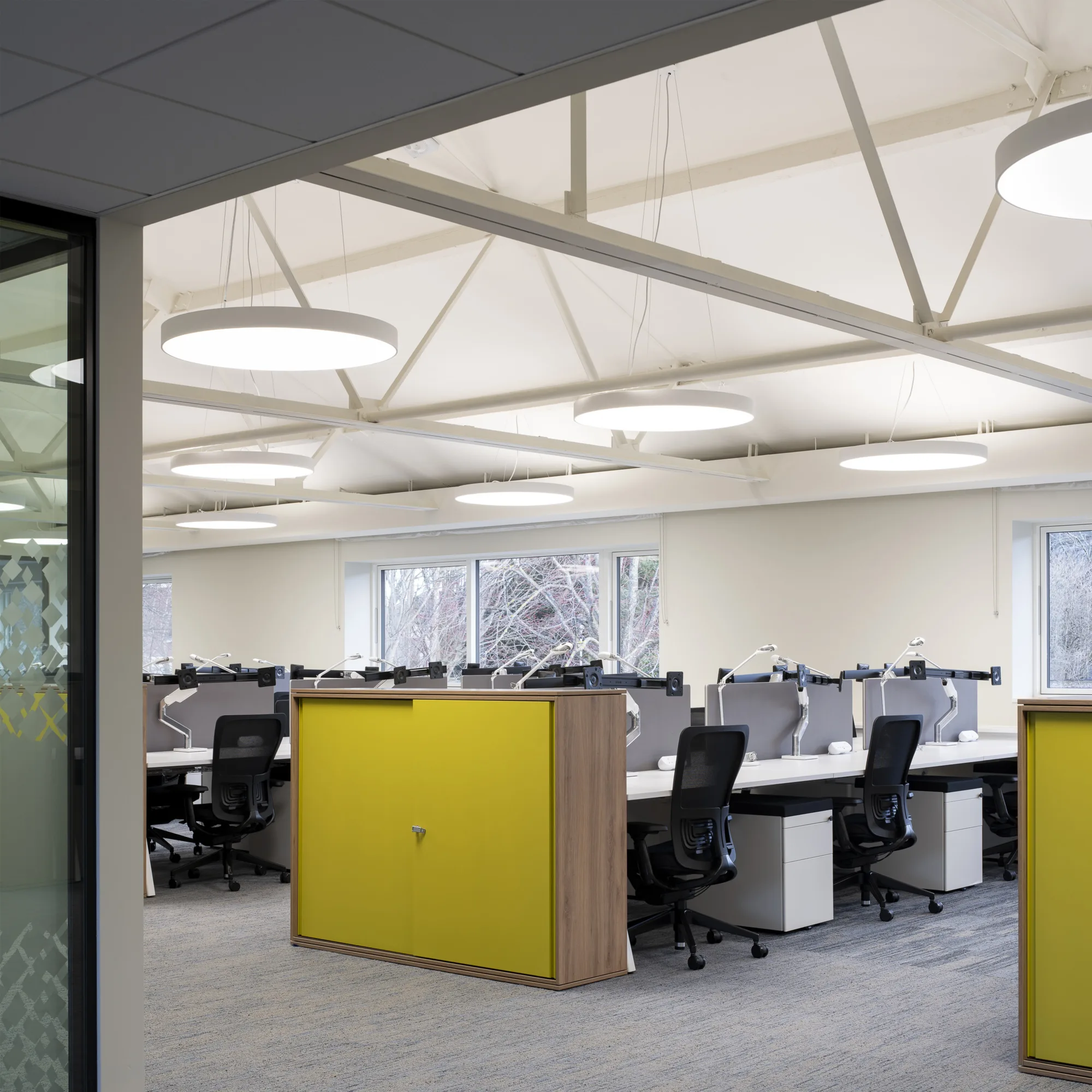 Angled side view of the open plan office with brightly coloured desk ends, black desk chairs and light walls and carpet