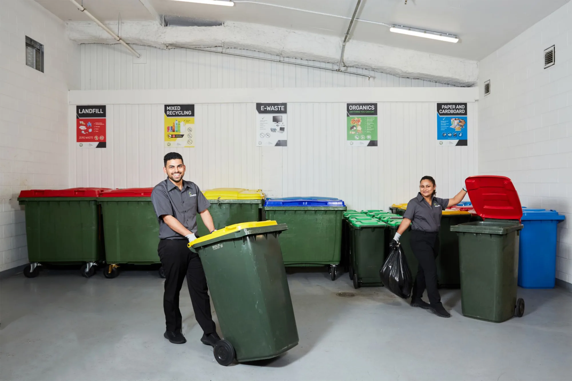 Bin storage room, man smiling with wheely bin, woman disposing of rubbish in another