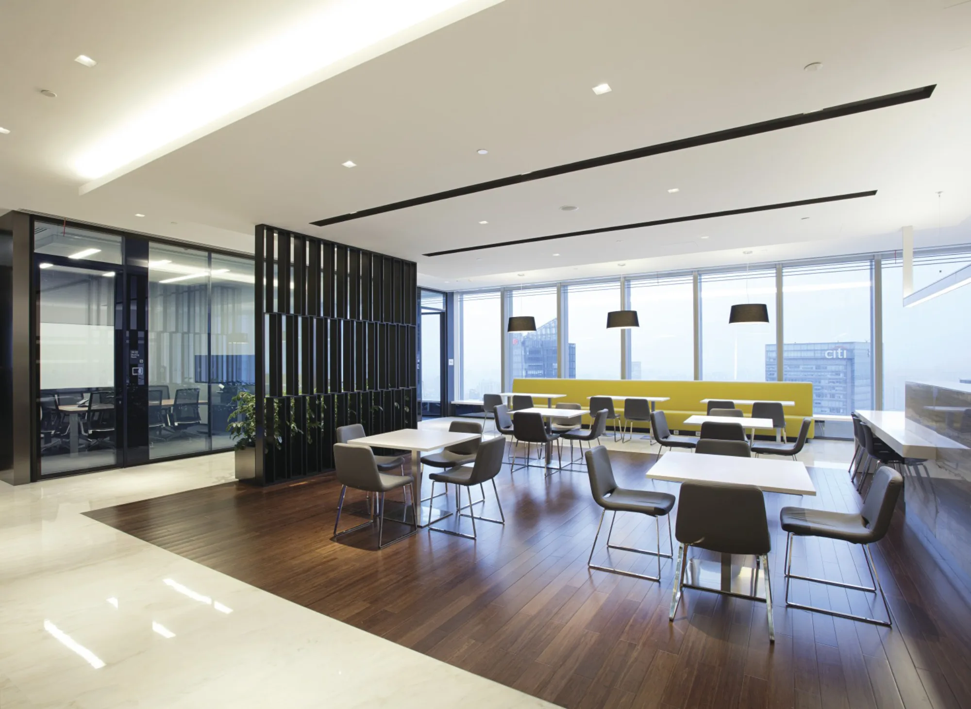 Collaborative workspace featuring array of square tables on wooden flooring and floor-to-ceiling windows