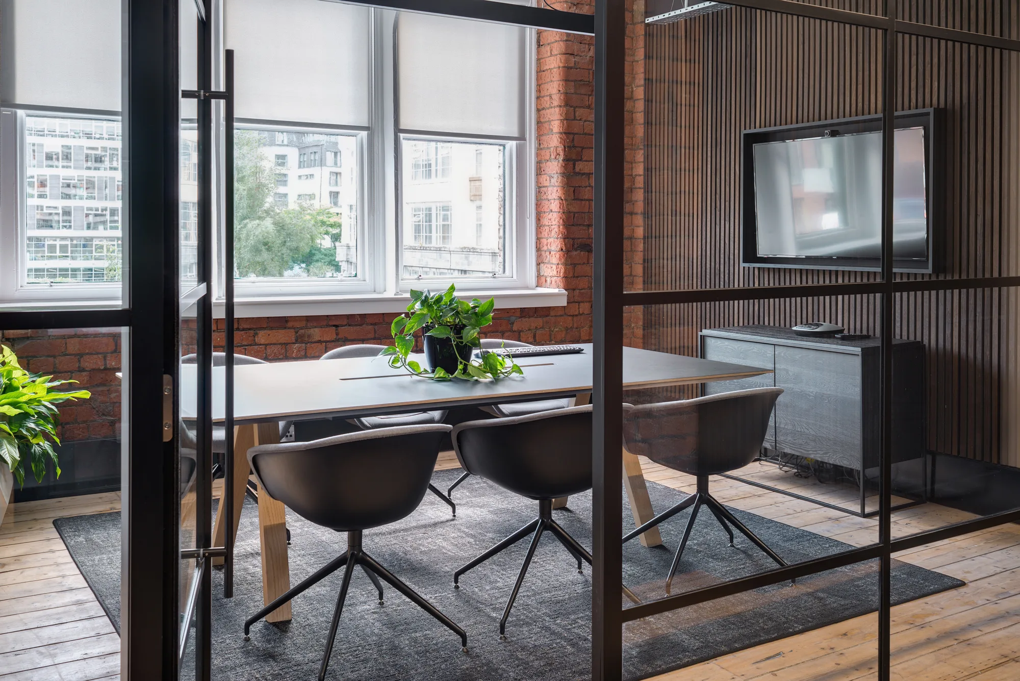 Glazed office meeting room with the door opened leading to a table with 6 chairs and a central green plant cascading from the pot.