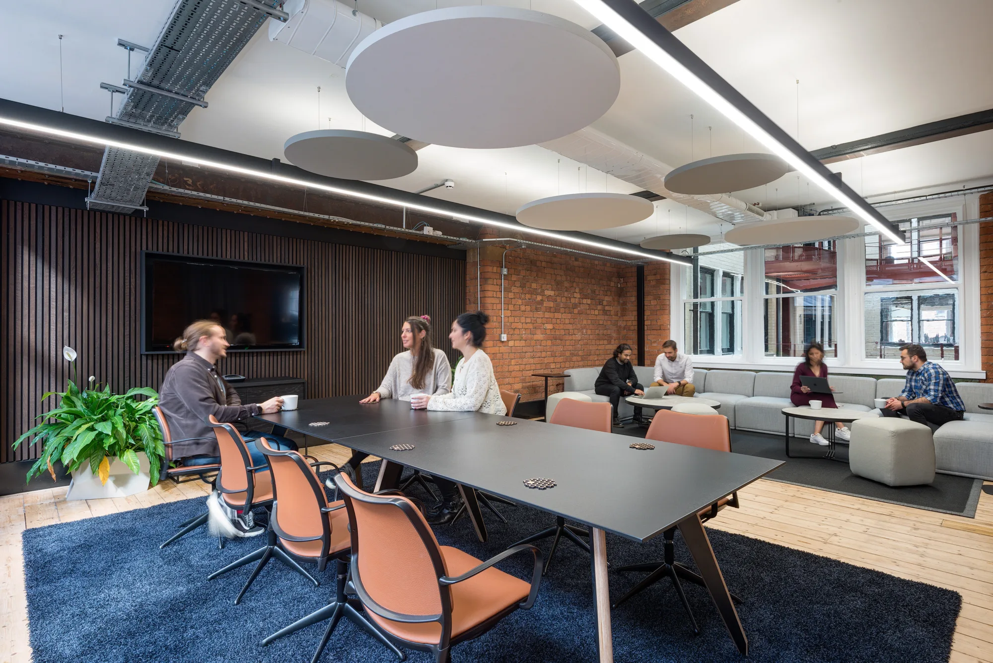 Breakout office space with large meeting room table on a blue rug and grey sofa seating