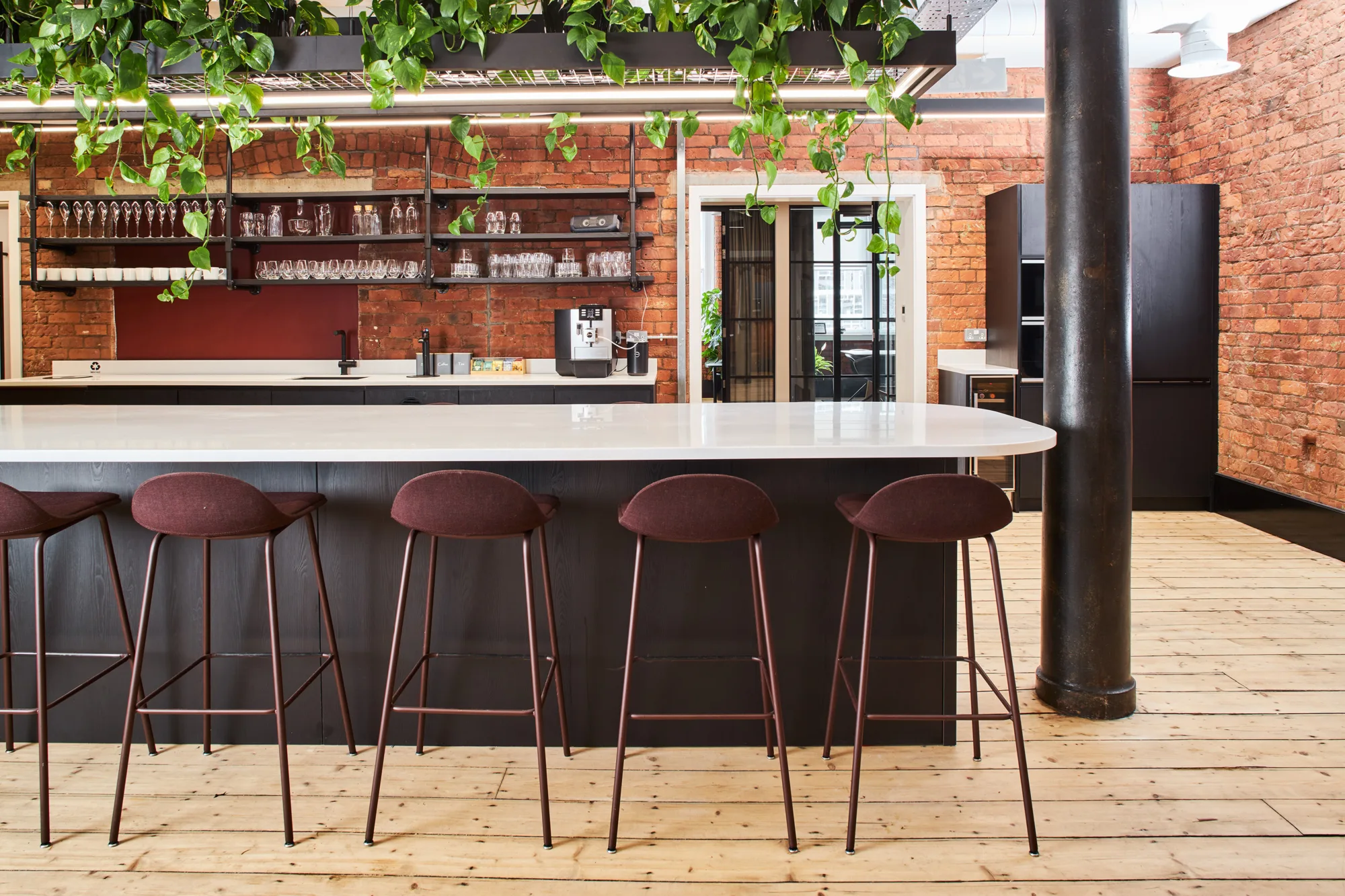 Kitchen island with tall stools on a wooden floor, exposed brickwork walls and hanging green plants