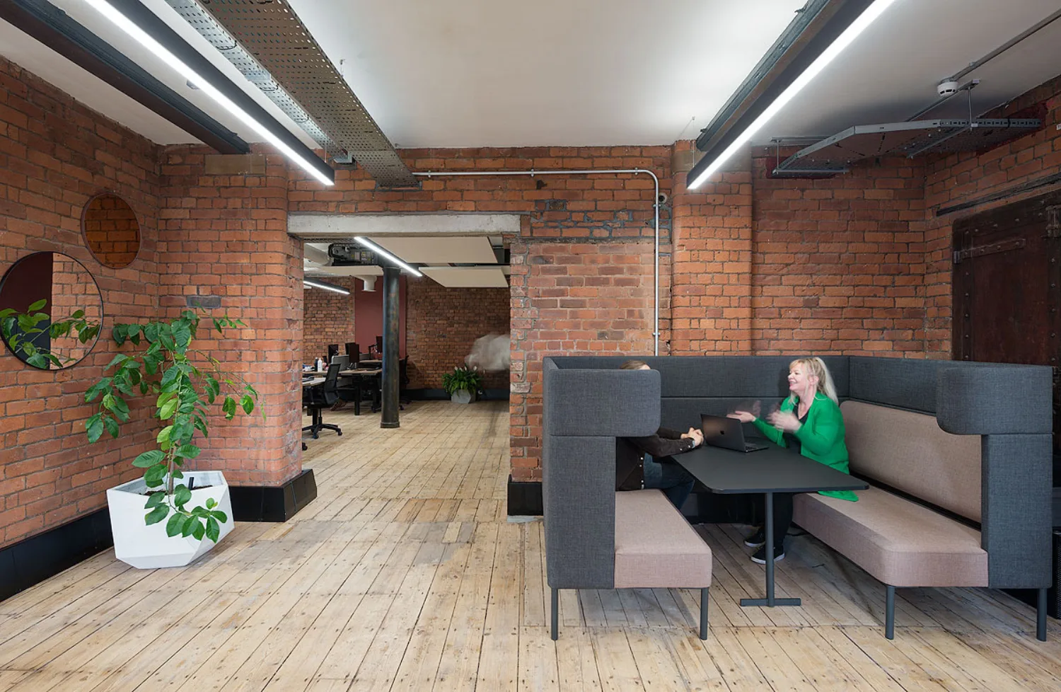 Occupied seating booth in the office space with wooden plank floors and exposed brick walls.