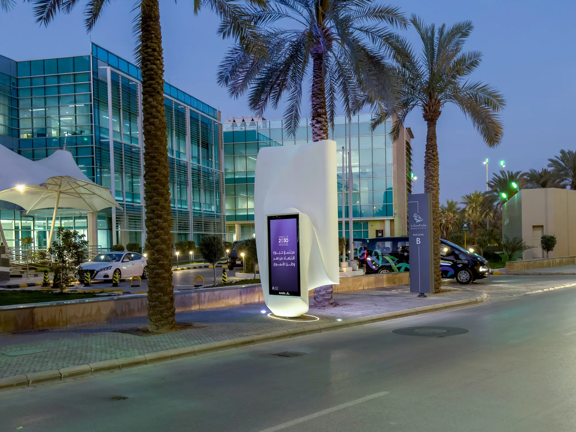 The digital advertising sculpture photographed from LCD screen side during evening time next to an office building