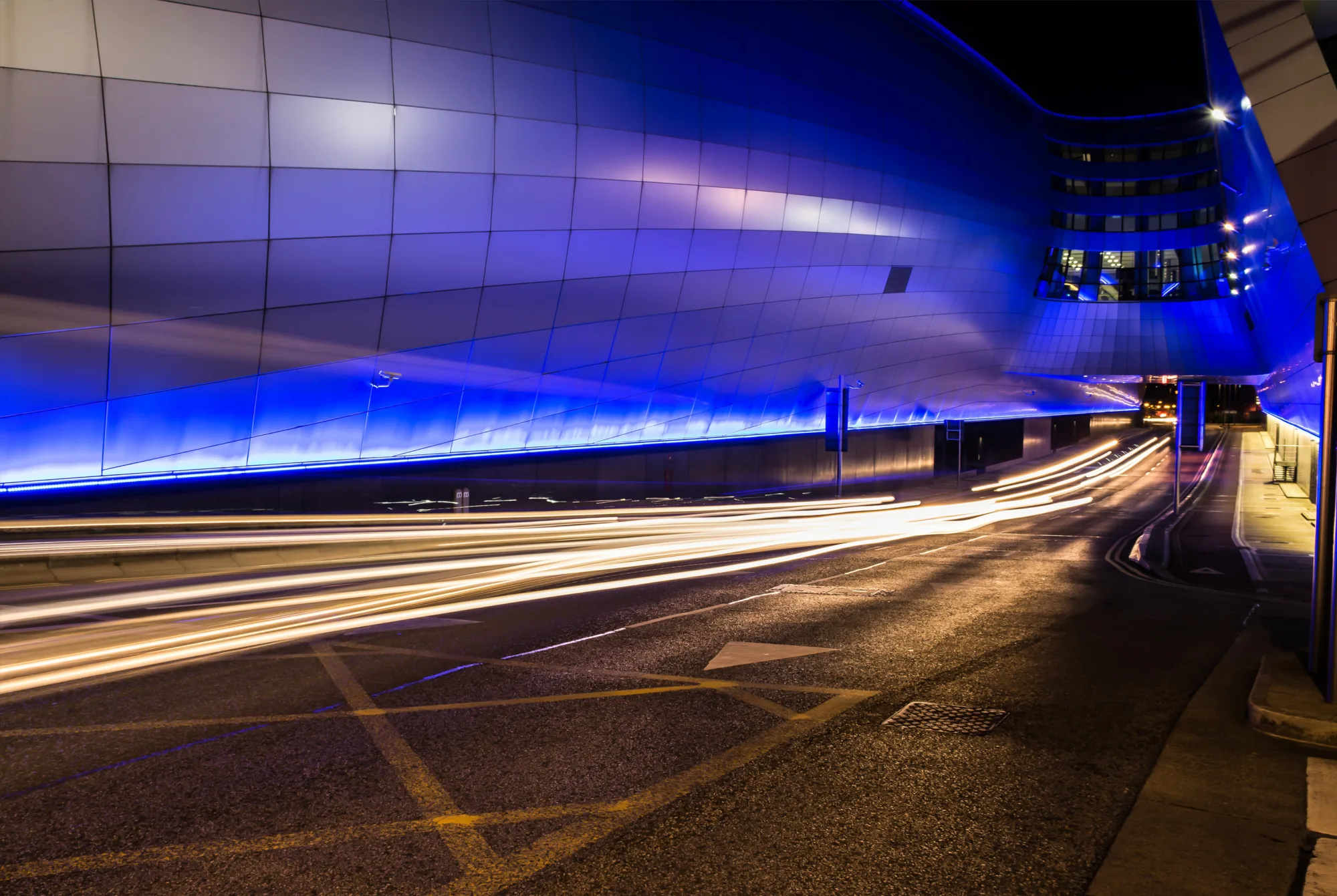 Road into an airport lit by blue lights and long-exposure car lights