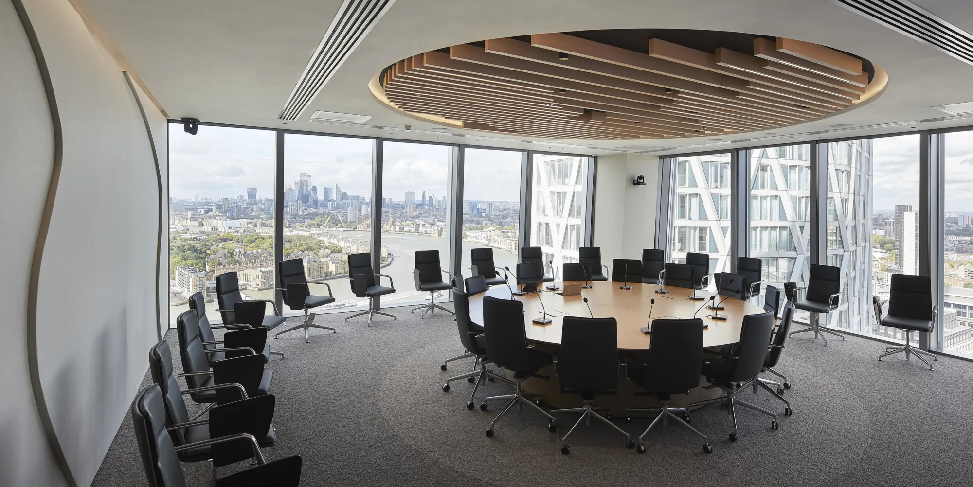 Meeting room with large central circle table with chairs around and chairs around the outside of the room, glazing on 2 sides