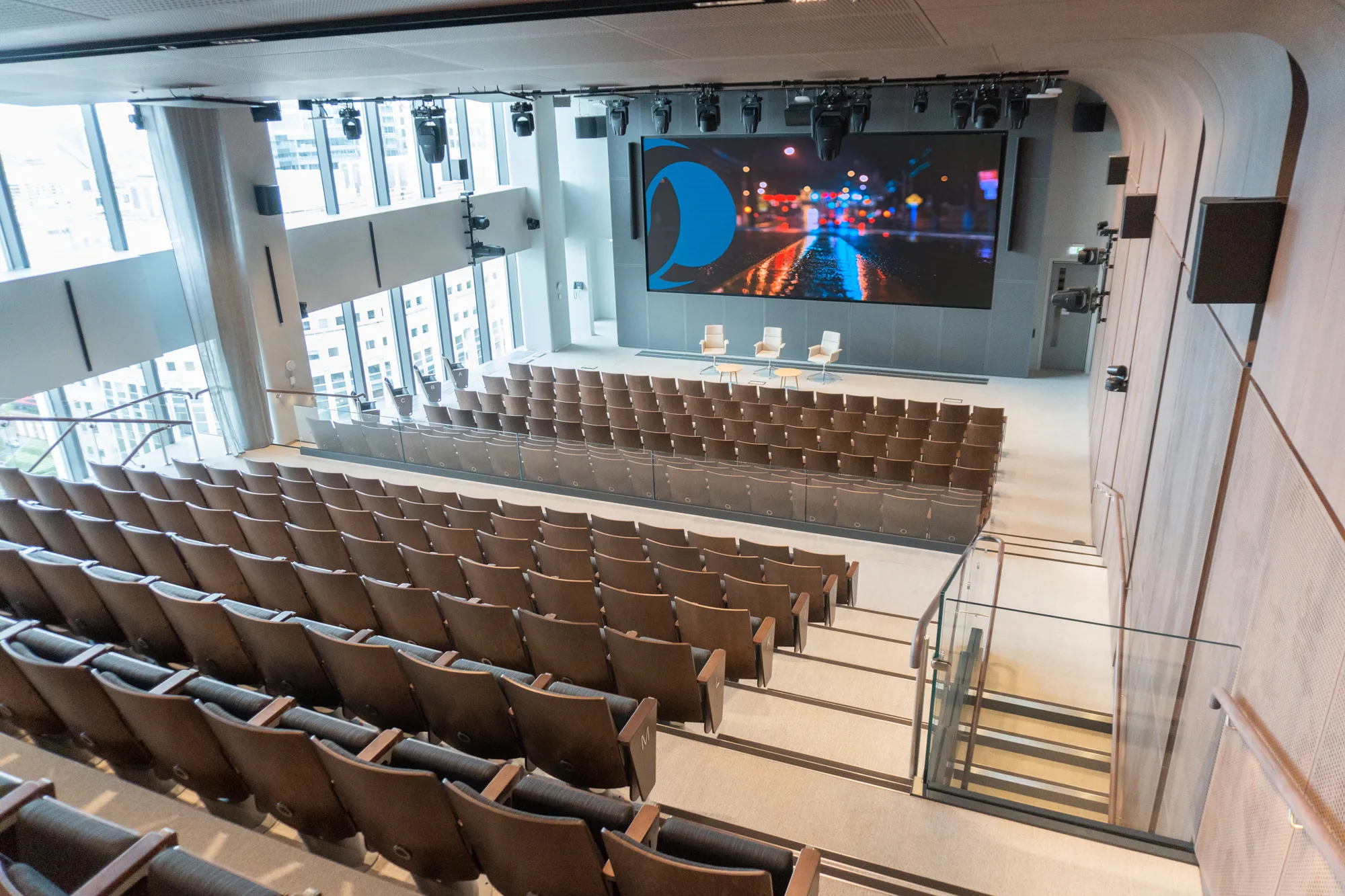 Auditorium shot from back of room, tiered seating with screen at one end, windows on left hand side