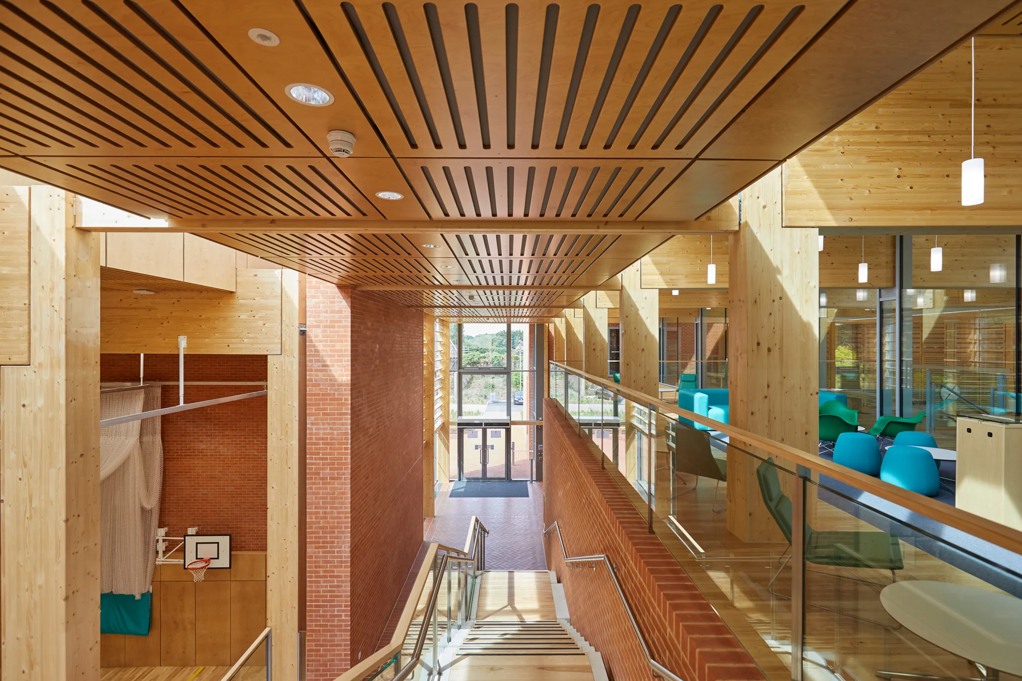 View front top of main stairs looking down passed reception to the front door with a glimpse of a sports hall to the left and seating area to the right.