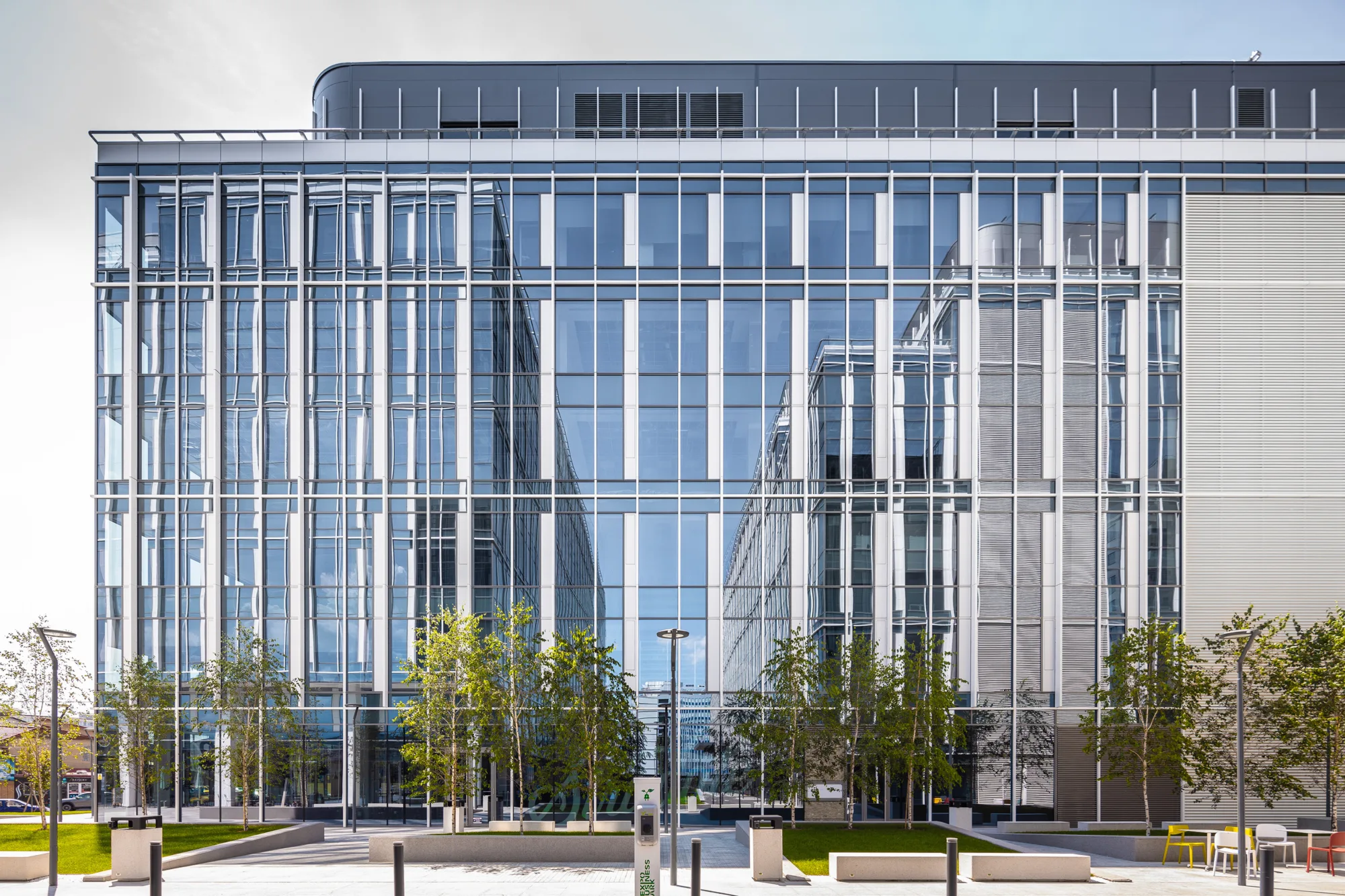 Glazed building in the background with trees, pedestrian walkways and bollards in the foreground