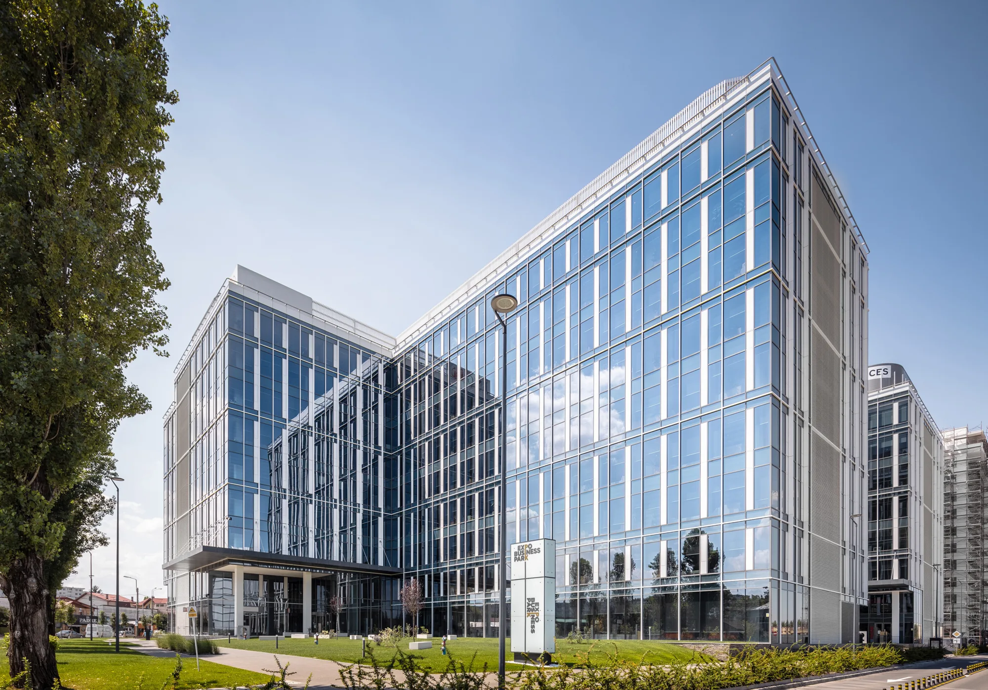 Glazed building with grass and a tree in the foreground with blue skies