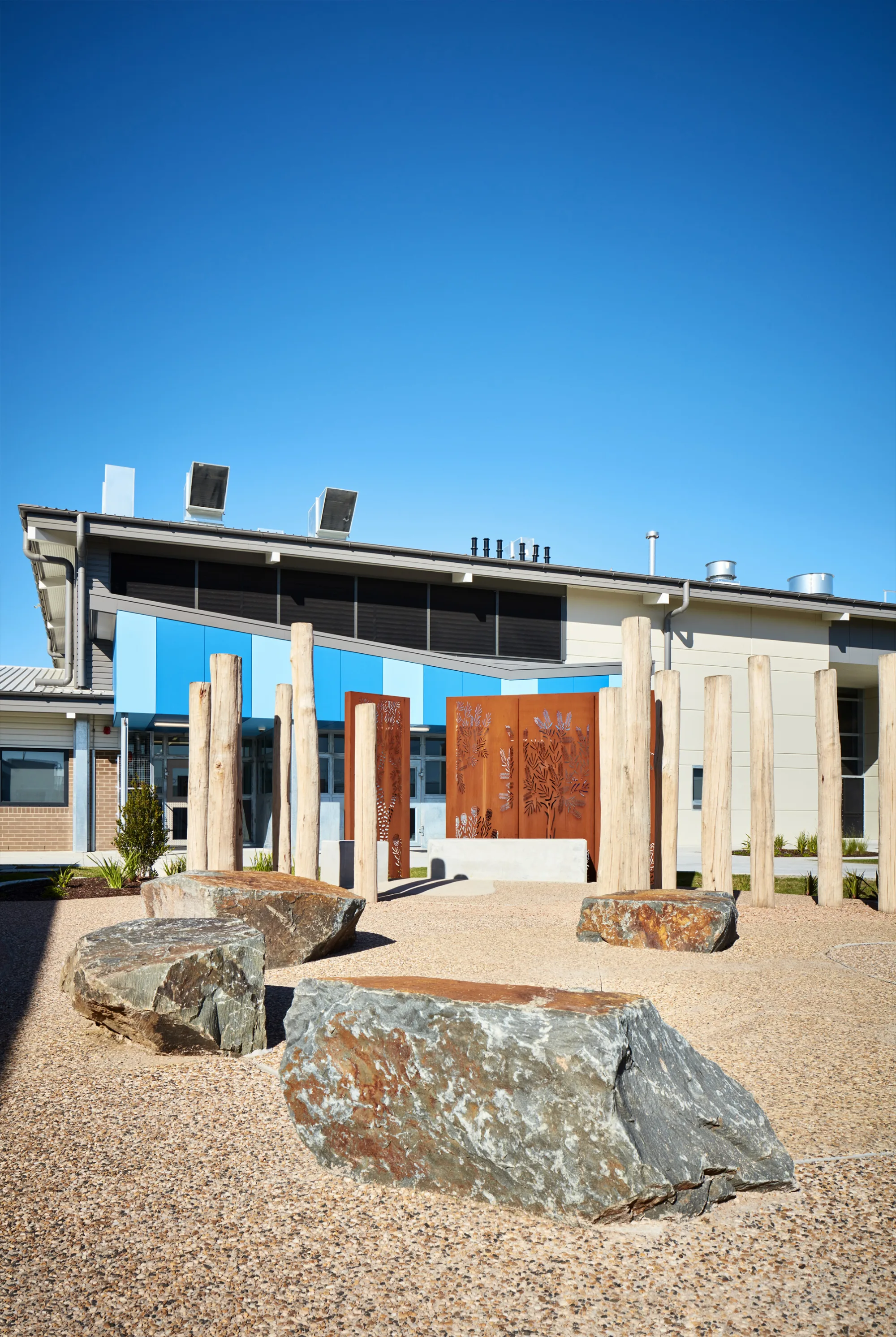 Outdoor meeting place with large rockery, wooden sculpture and rusted metalwork feature wall.