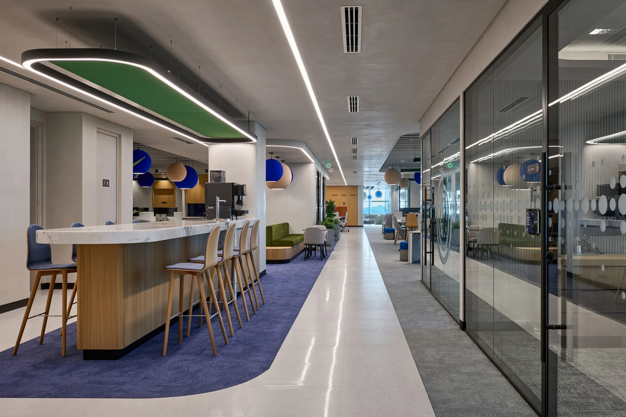 Informa office walk way with kitchen bar stool area on the left and meeting rooms on the right with the rest of the office in the background.