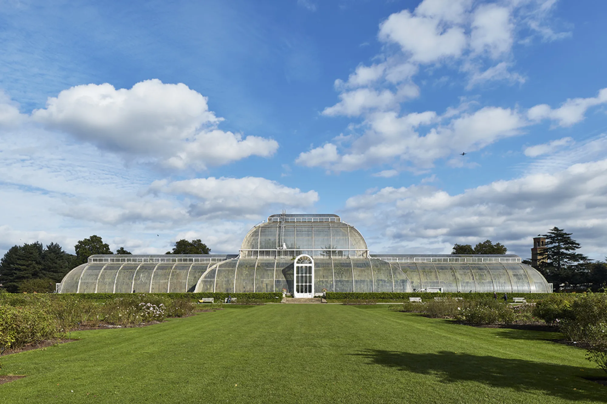 Kew Gardens Palm House with lawn in front of glass building with cloudy blue sky
