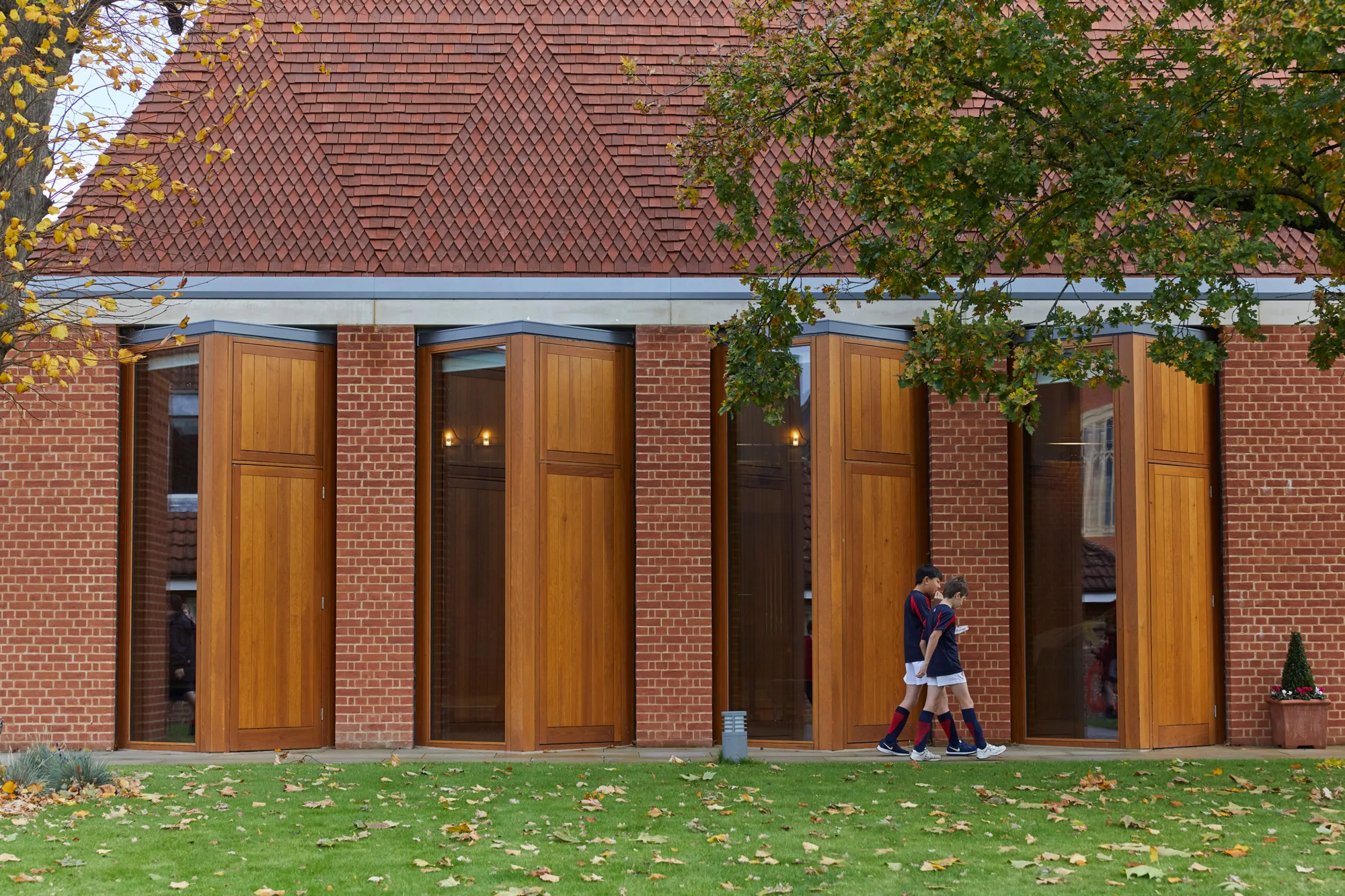 2 students walking past the timber, brick and glazed exterior of the music hall