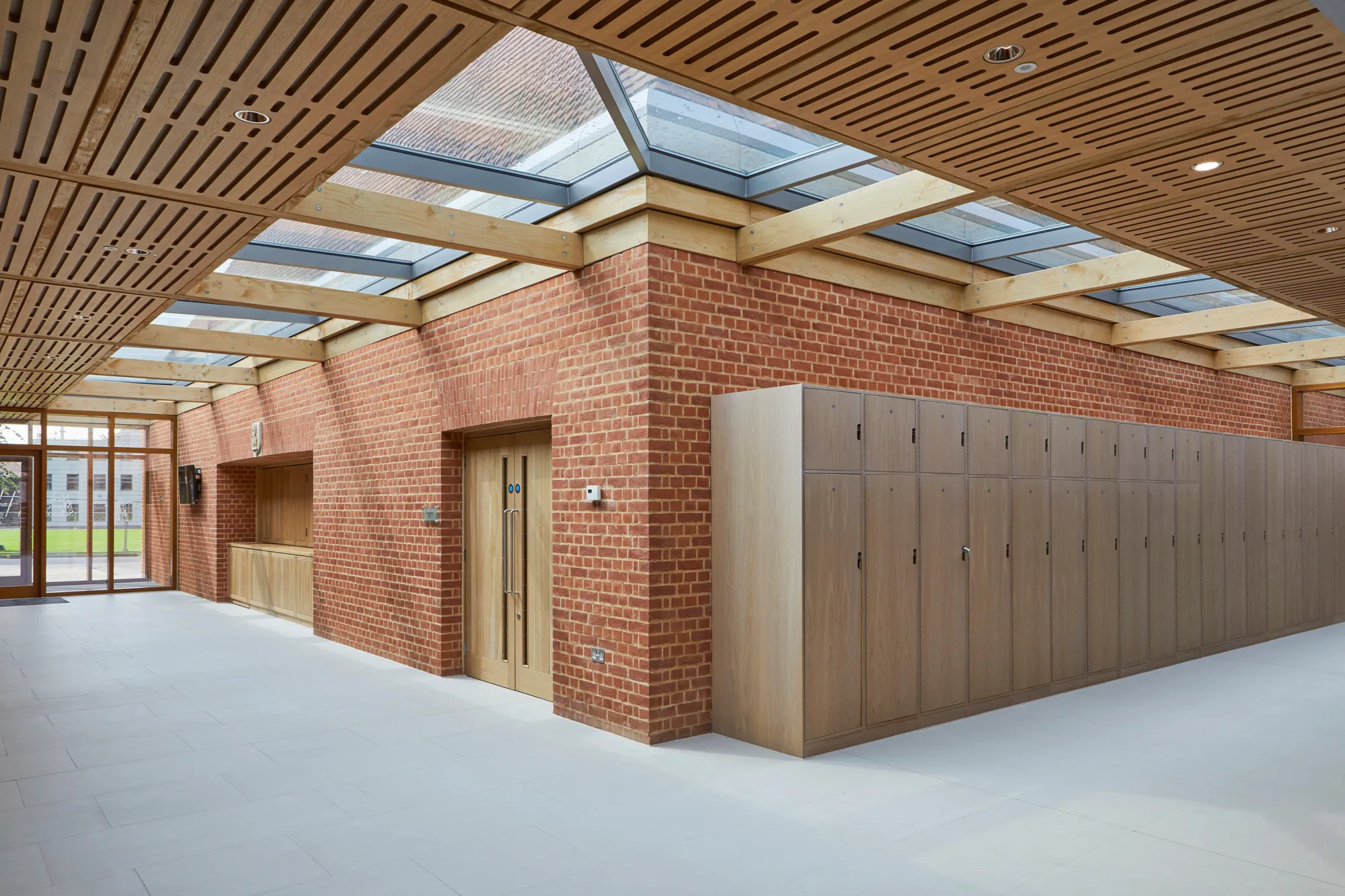 Interior of the building corridor with wooden lockers lining the brick wall under a timber and glazing ceiling