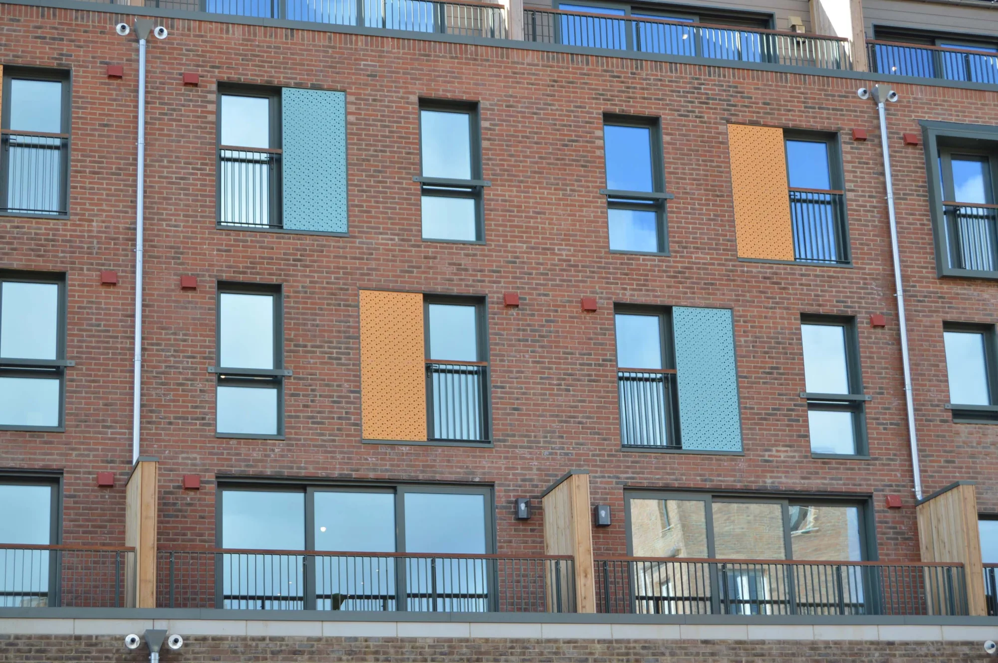 Brick facade of the apartments with glazed windows with blue and orange adjacent panels
