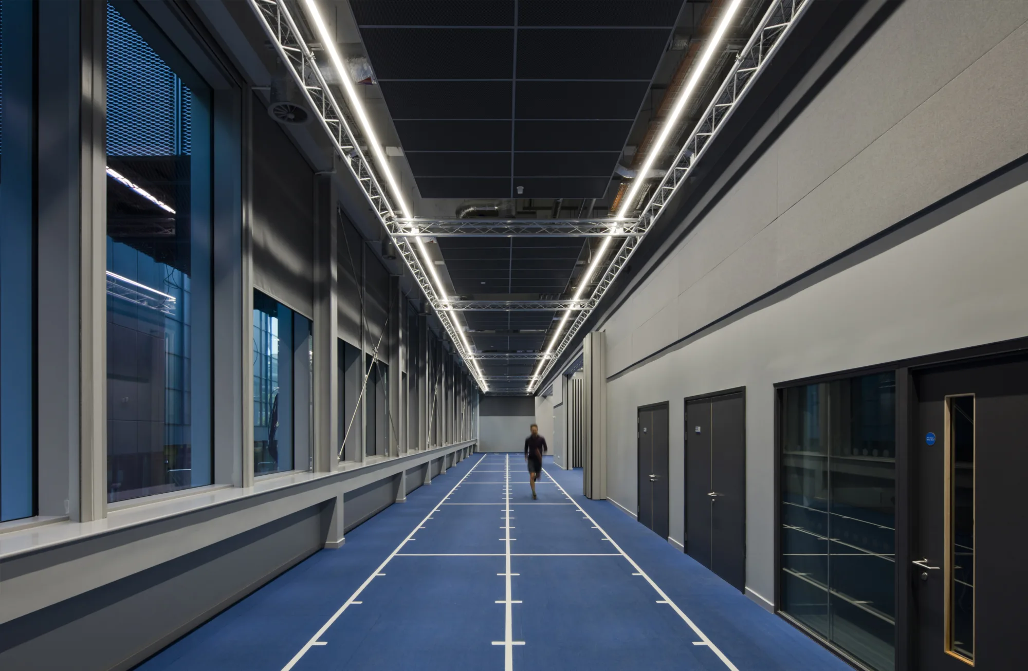 Interior of a blue running track inside a narrow grey corridor