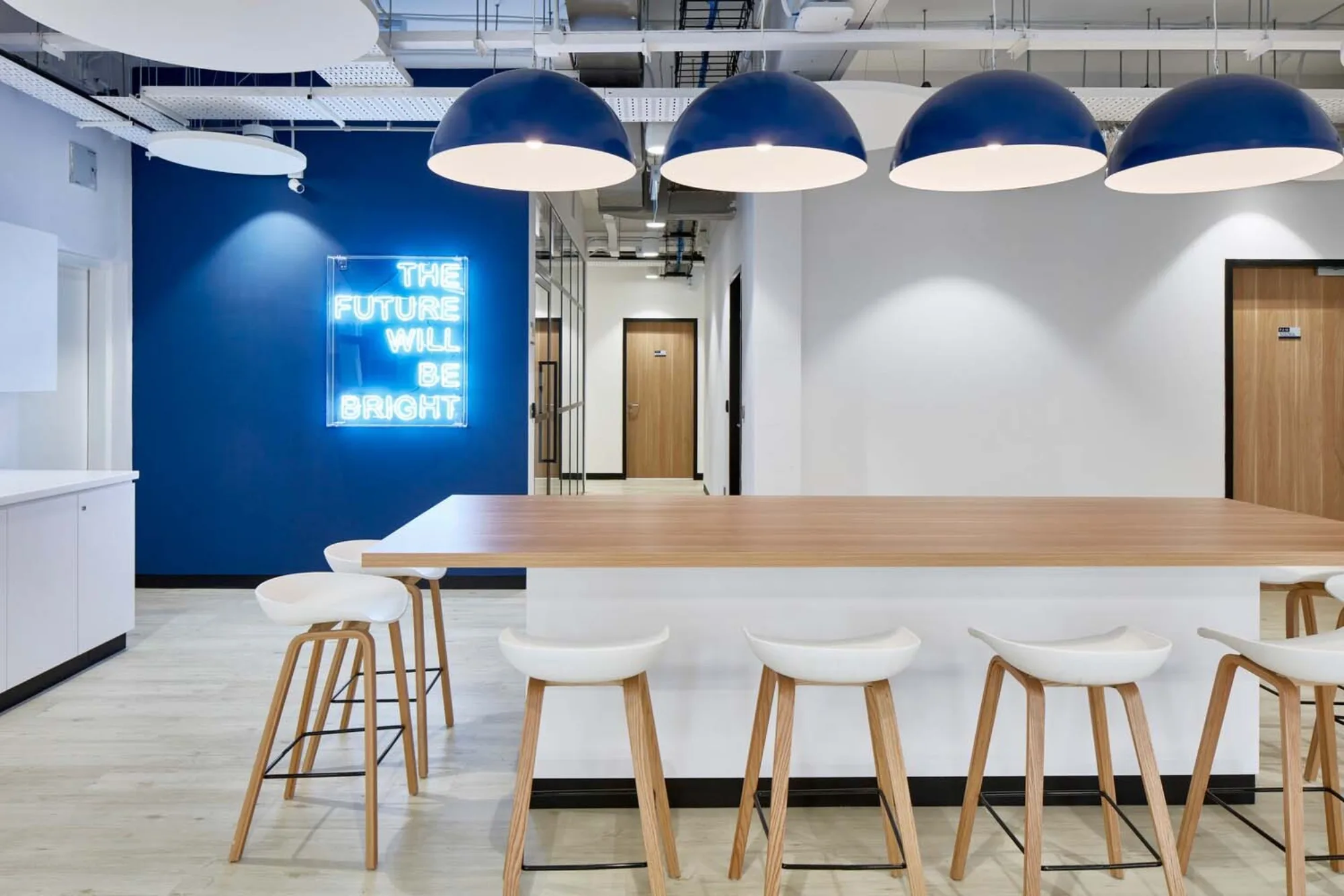Large rectangular table with high-top chairs and overhanging lights; LED light decor beside hallway in the background