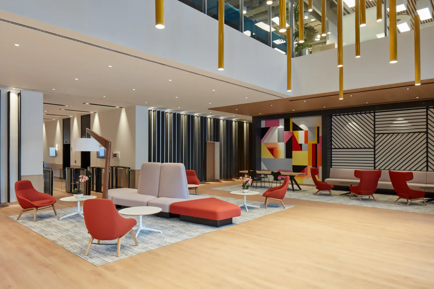 PWC Middle East large guest and meeting area with ample amount of desks and chairs while being illuminated by artistic chandeliers. A smart, secure and modern bio metrics entrance is also visible.