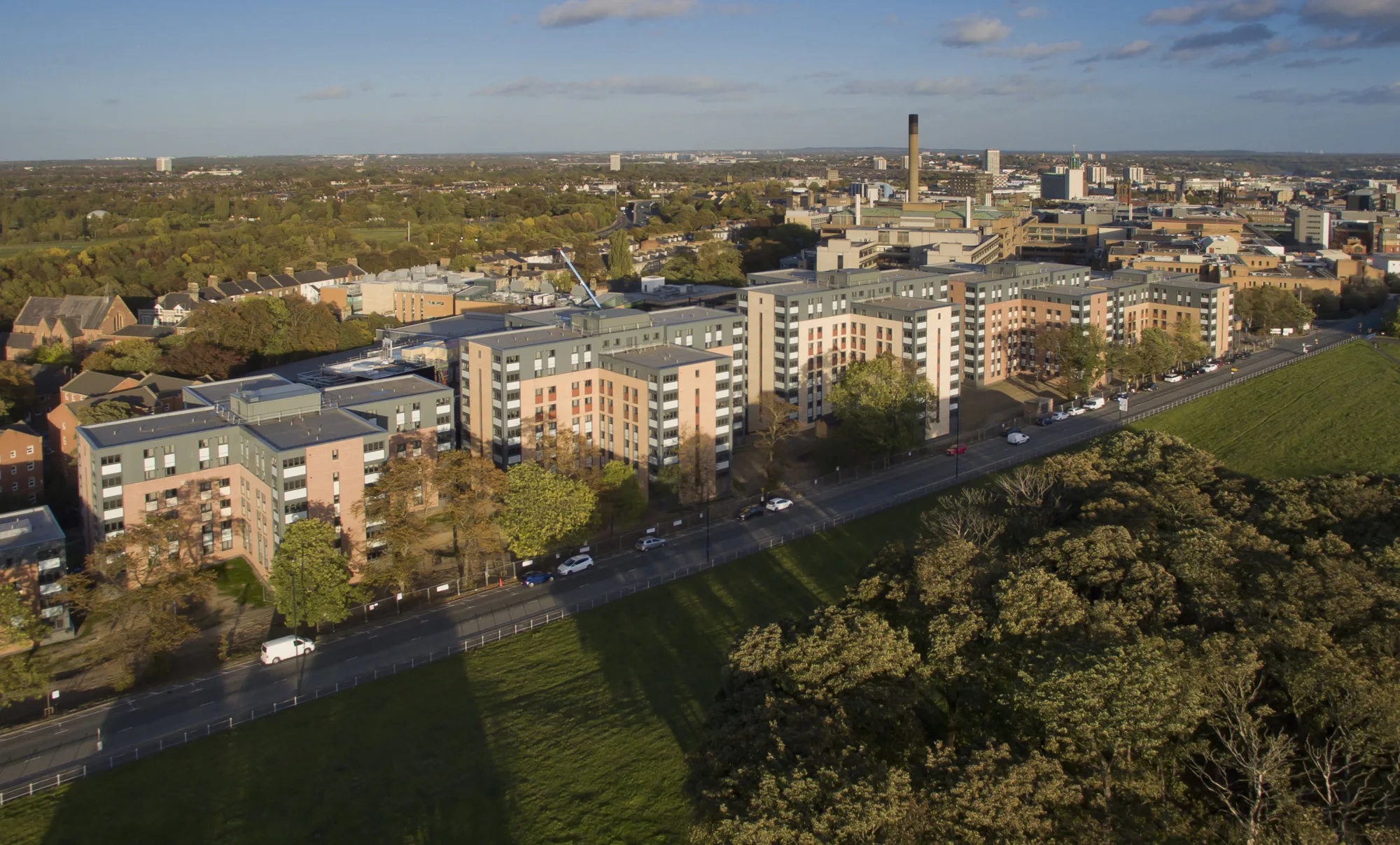 Overhead view of the student village - several similar multi-storey residential buildings with dark grey and light brown exterior surrounded by other buildings, a road and a field.