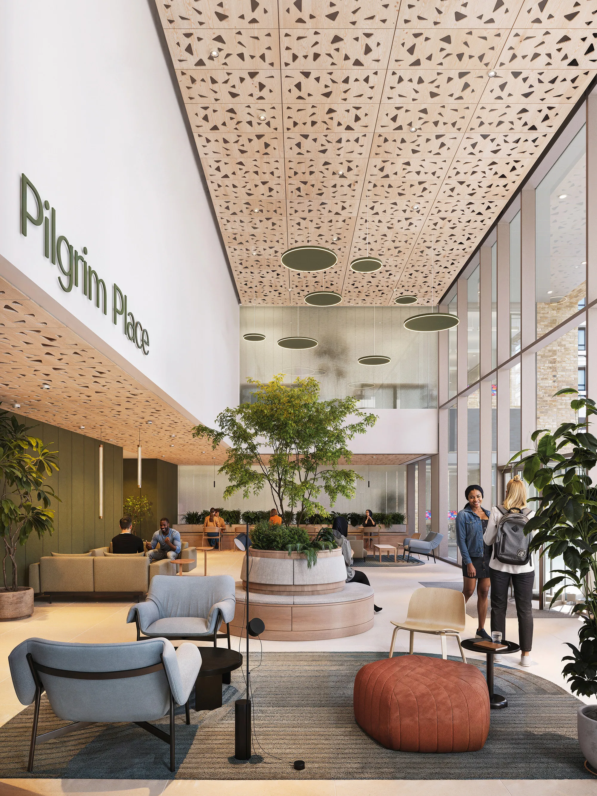 Lobby area with high patterned ceiling, large windows, and seating including chairs and poufs. A round planter with a tree is centered. Visible text reads “Pilgrim Place” on the left wall. Several people are standing and sitting throughout the space.