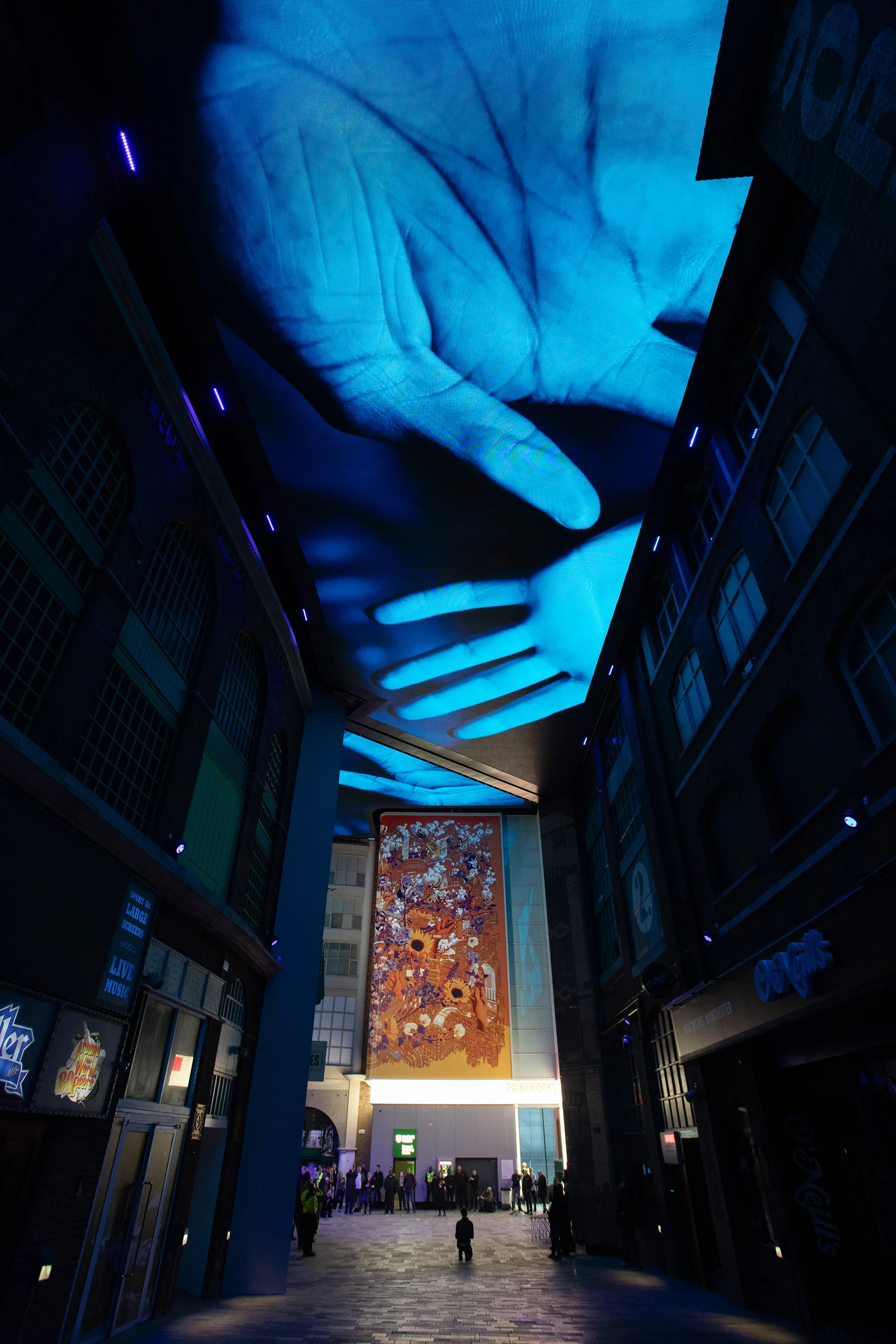 Blue tinted hands projected on the ceiling above the dark indoor alley way