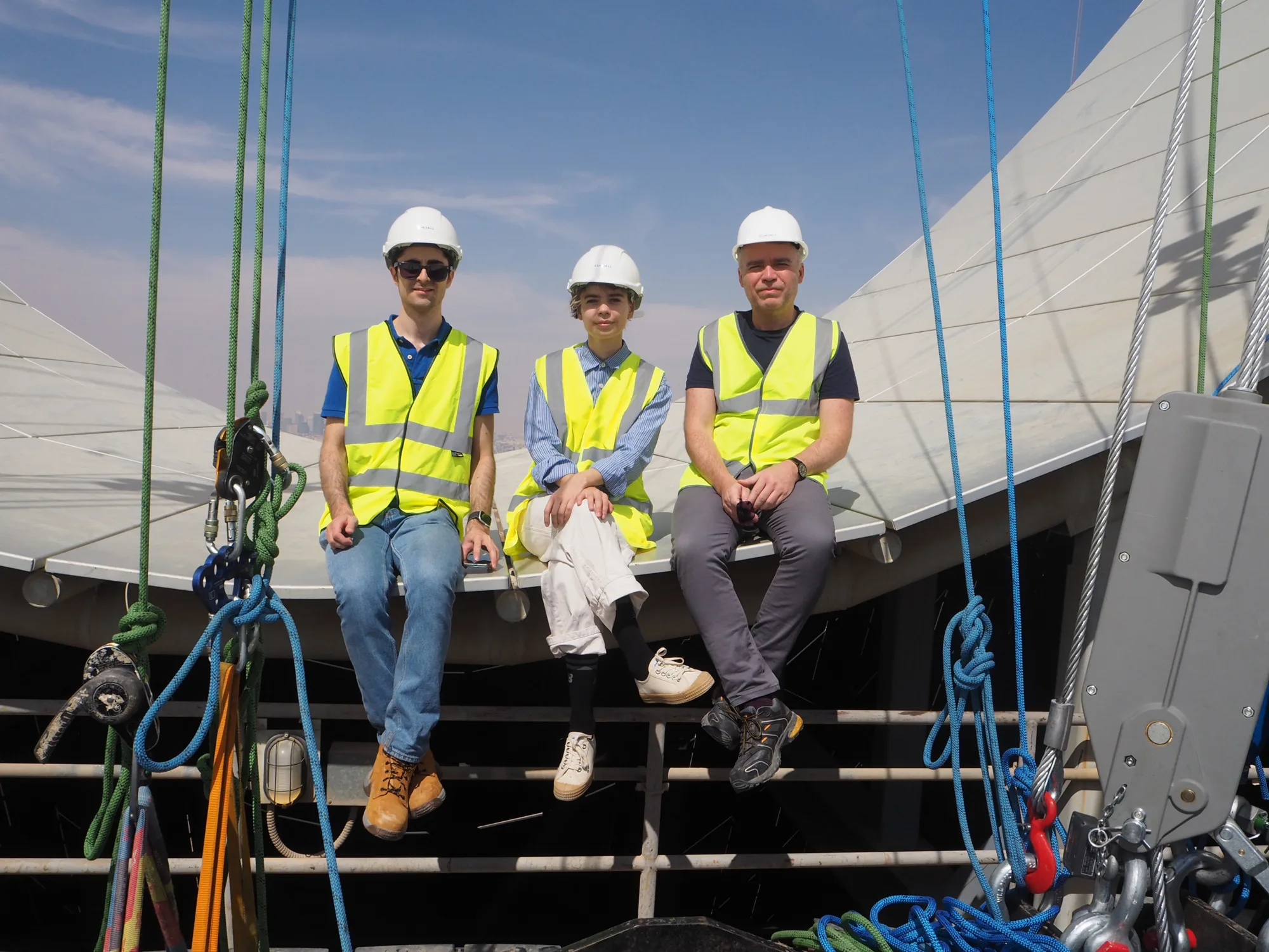 Three of the team in PPE sat on the curve of the building looking to camera