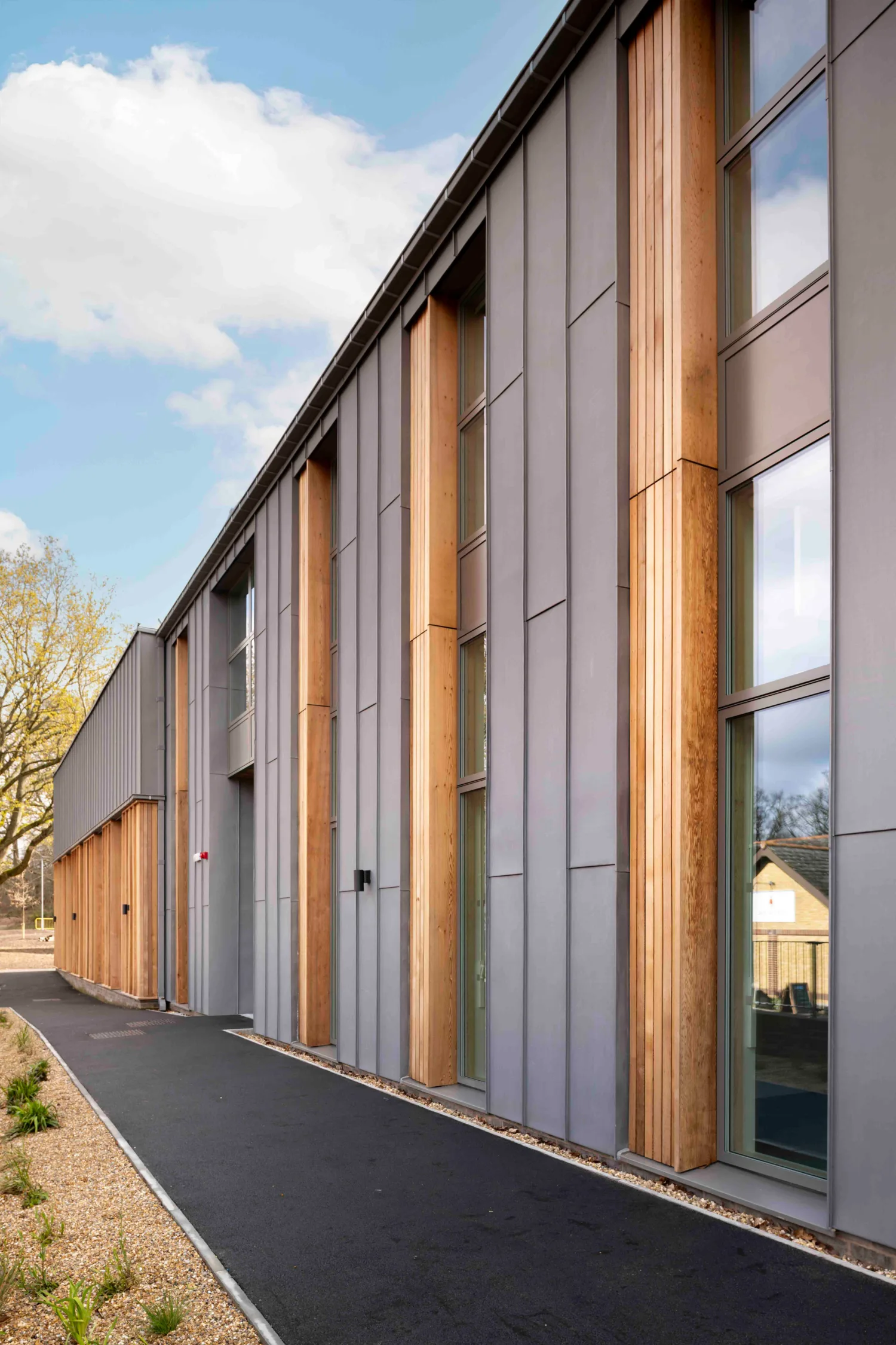 Exterior view of the side of Royal Military Academy Sandhurst Music Facility featuring grey metallic panels and wooden accents
