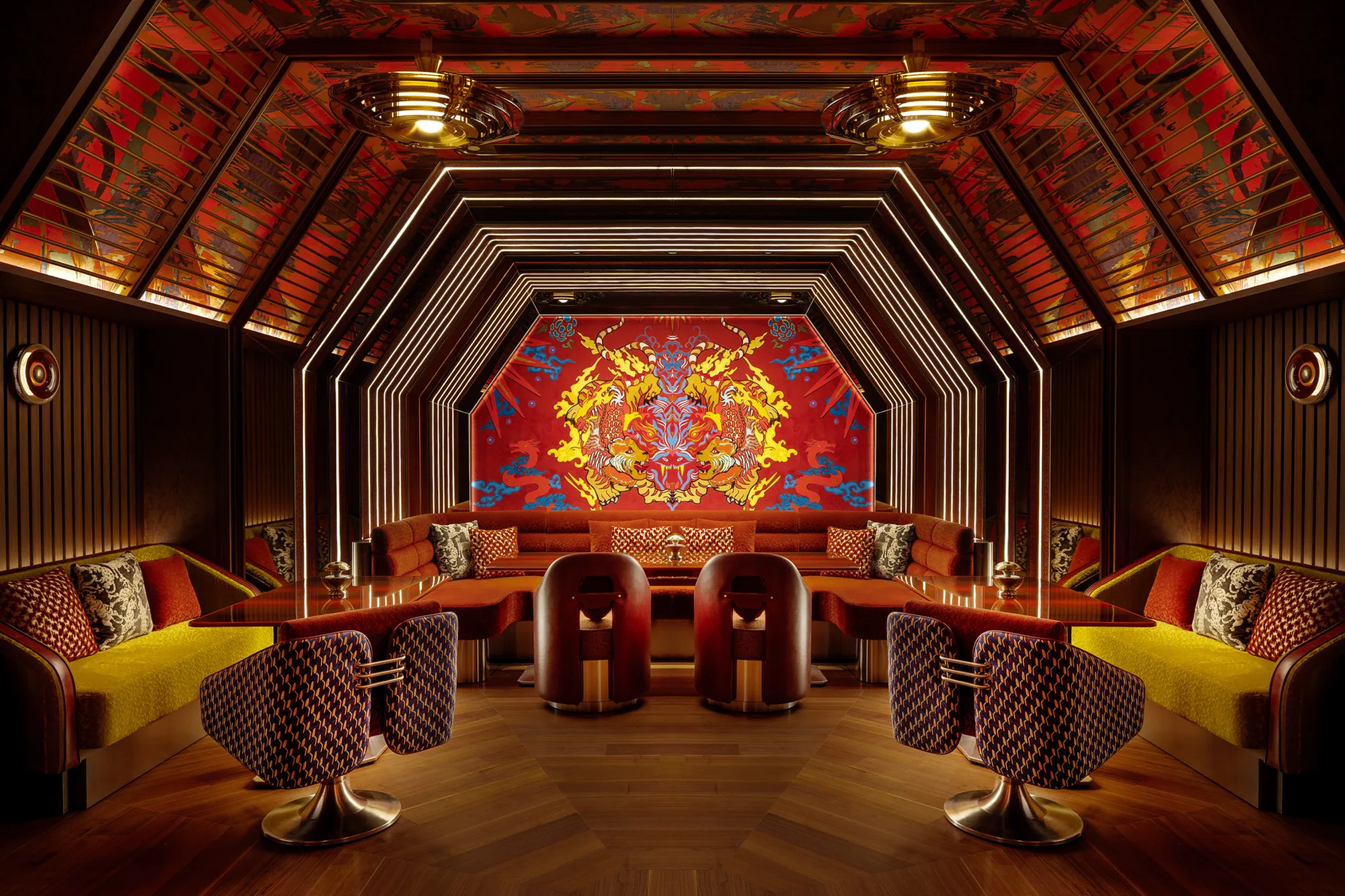 Interior of a dimly lit lounge with patterned chairs, cushioned benches, small round tables, and a vivid red and yellow symmetrical mural at the far wall, framed by angular wood and metal paneling.Interior of a dimly lit lounge with patterned chairs, cushioned benches, small round tables, and a vivid red and yellow symmetrical mural at the far wall, framed by angular wood and metal panelling.
