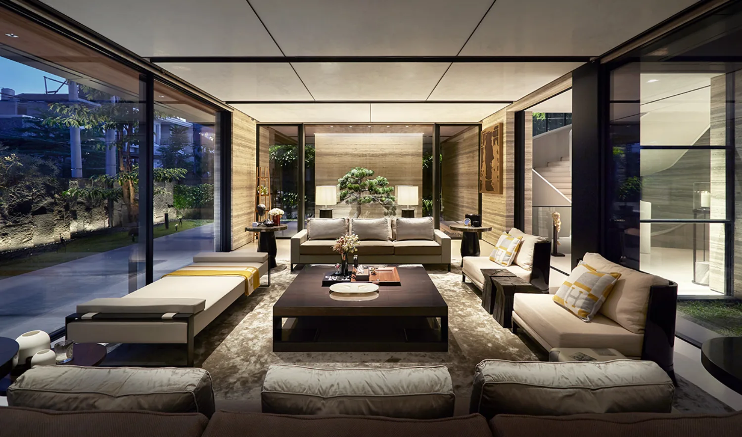 Lounge area with glass façade showing exterior space. Soft lighting with seating around the table