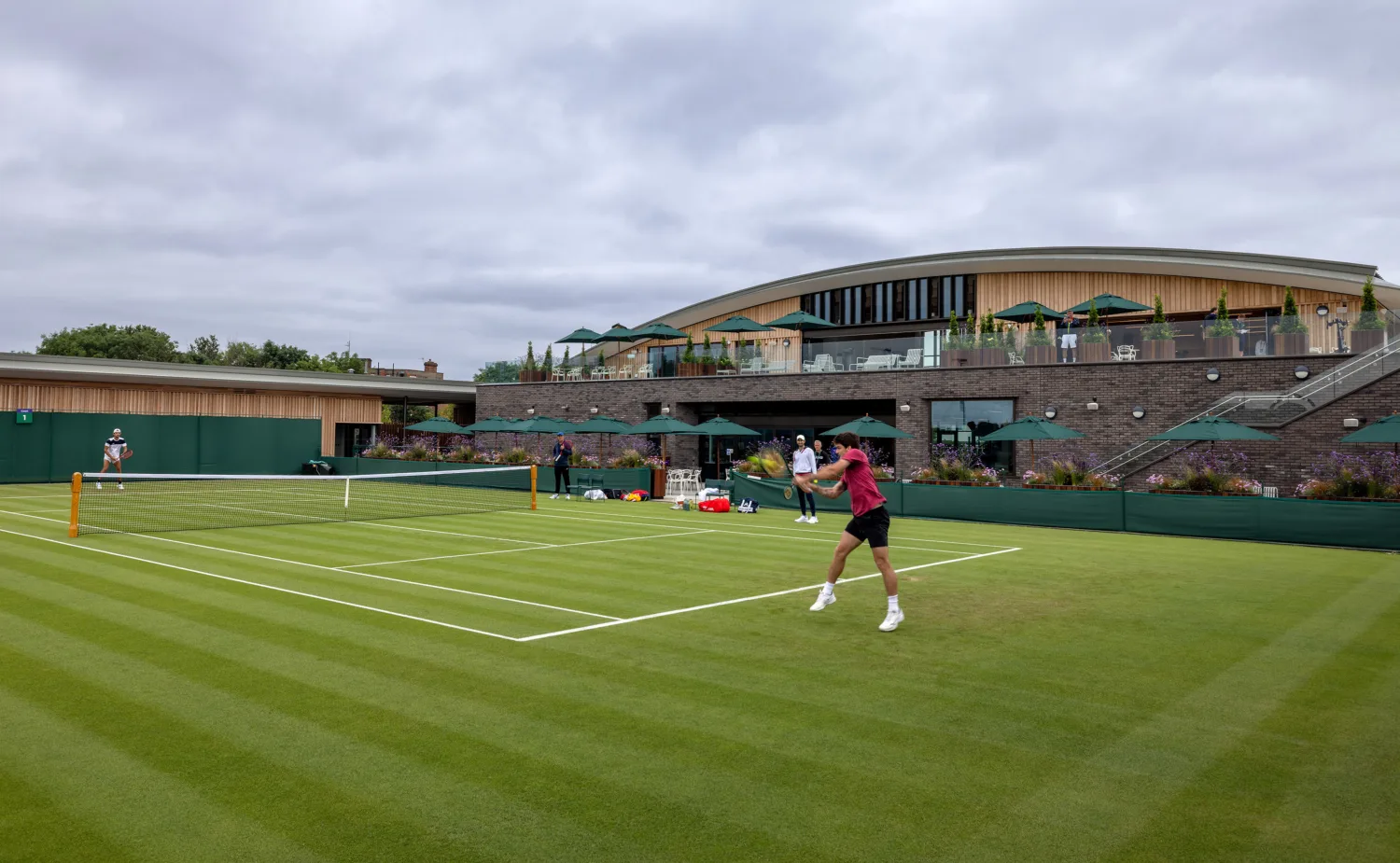 A match being played on a grass tennis court in front of the clubhouse