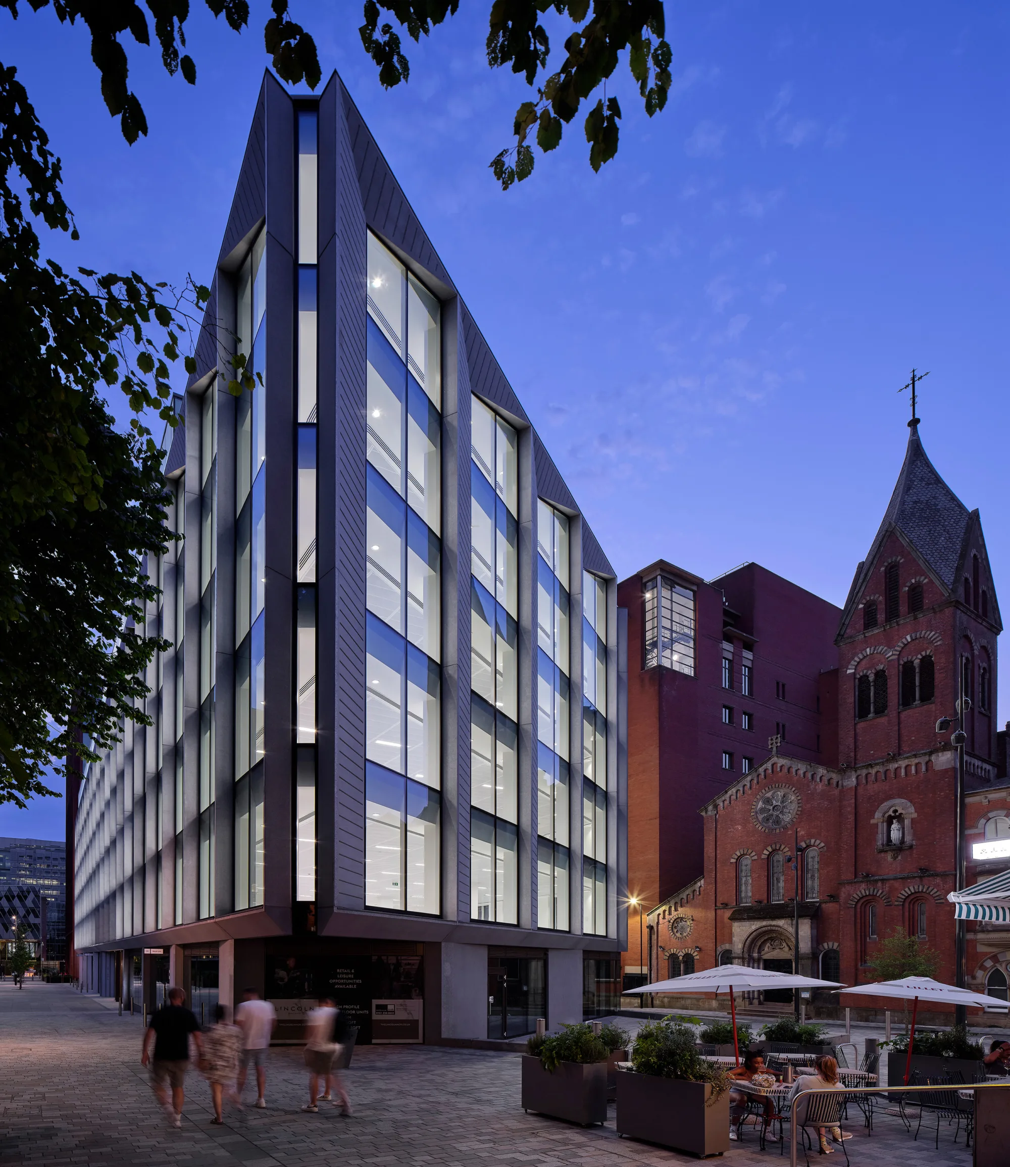Exterior of the building, with alfresco dining in the foreground and a brick church in the background