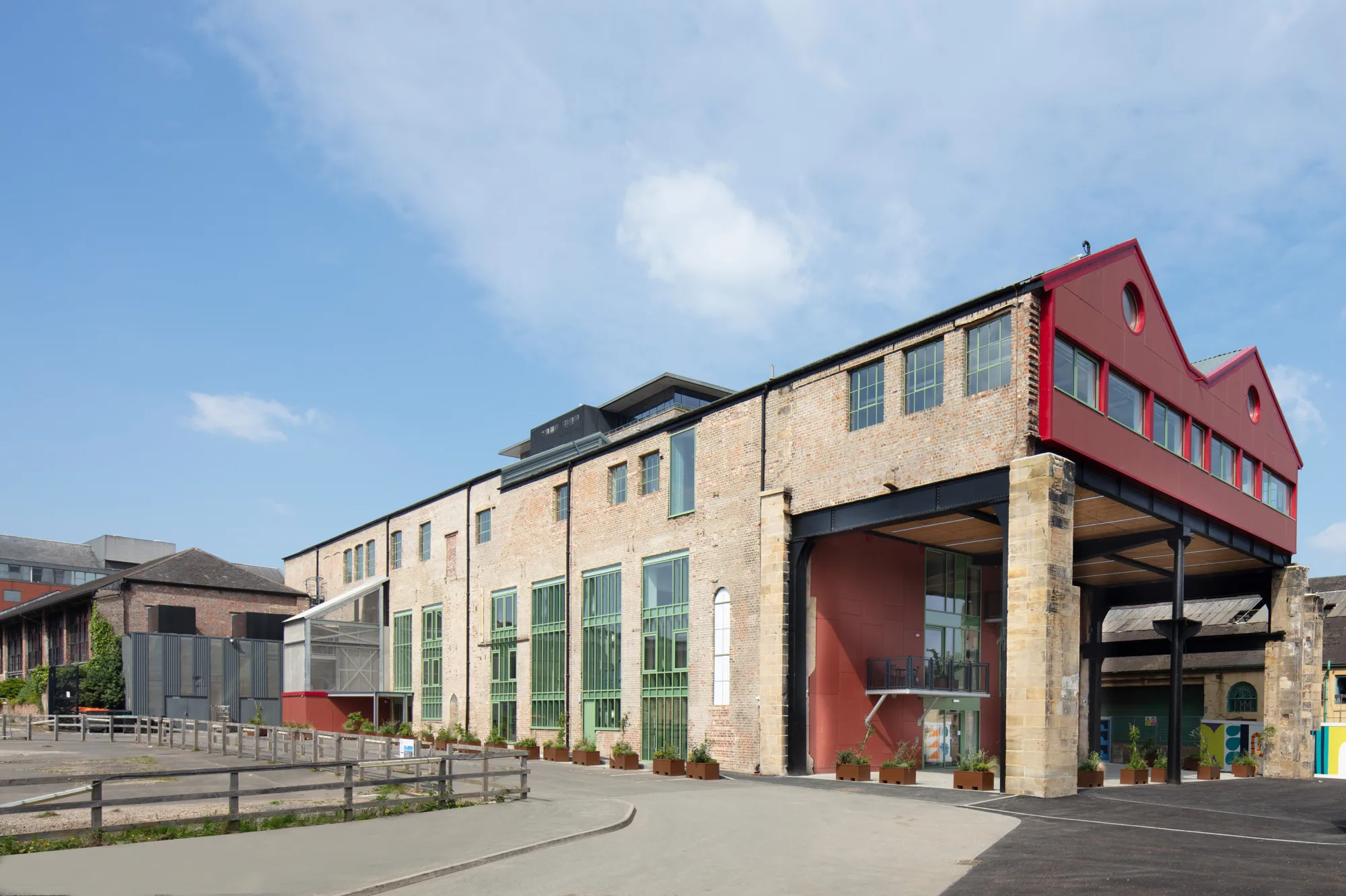 Outside of the building with red panelling on entrance wall and windows on right hand side. The windows on the left of the building have a green trim.
