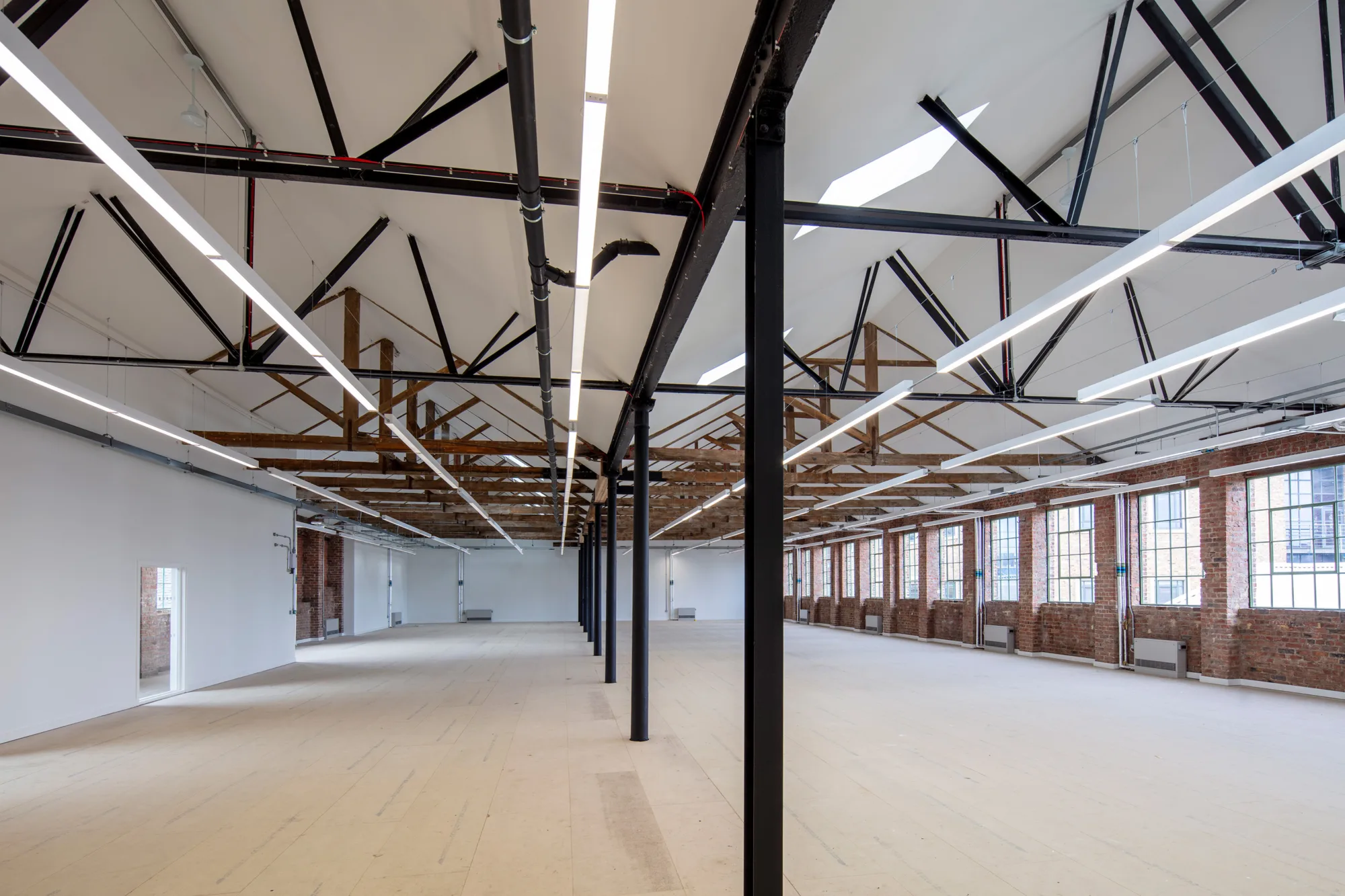 The main office space with black beams throughout the middle. Meeting rooms to the left with windows across the right hand side.
