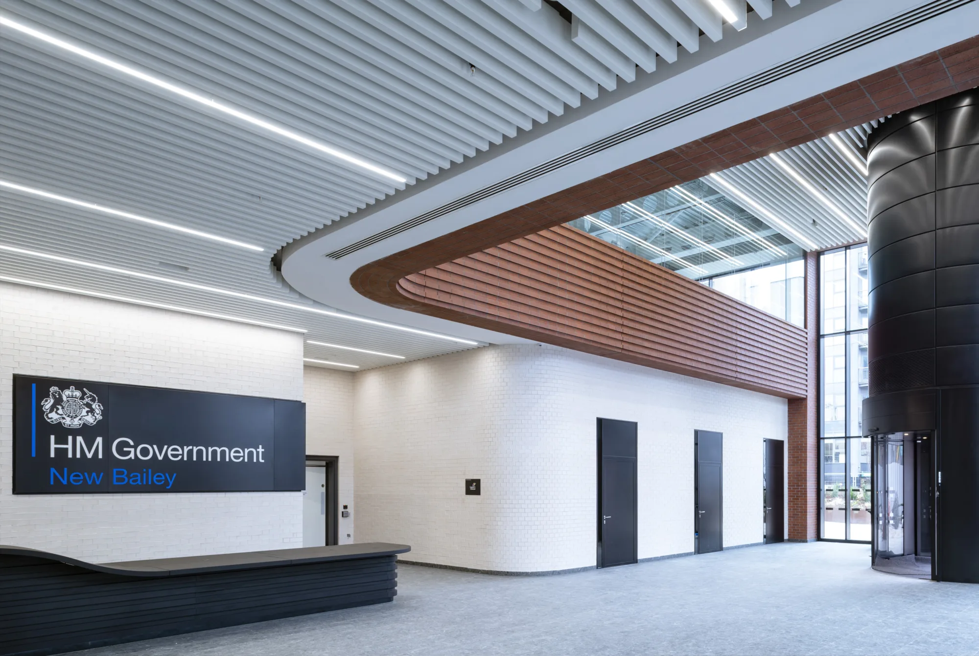 Interior lobby with white walls and ceiling and a black sign with white writing with the title 'HM Government'