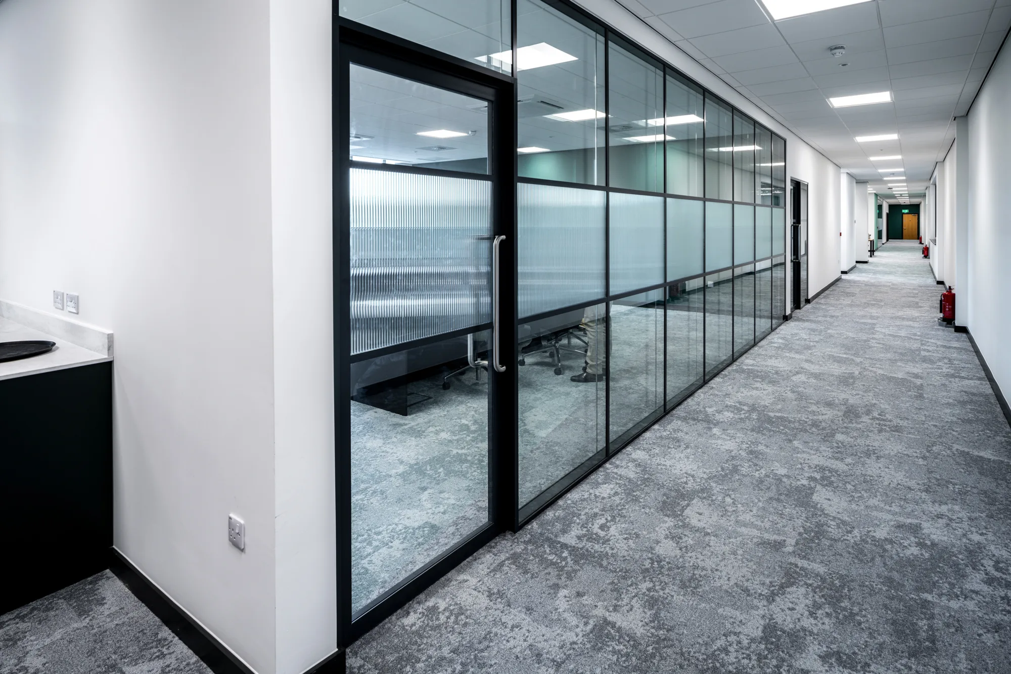 A long corridor with rooms alongside behind translucent glass windows, inside the Peak Pharmacy warehouse in the Tudor Cross industrial complex.