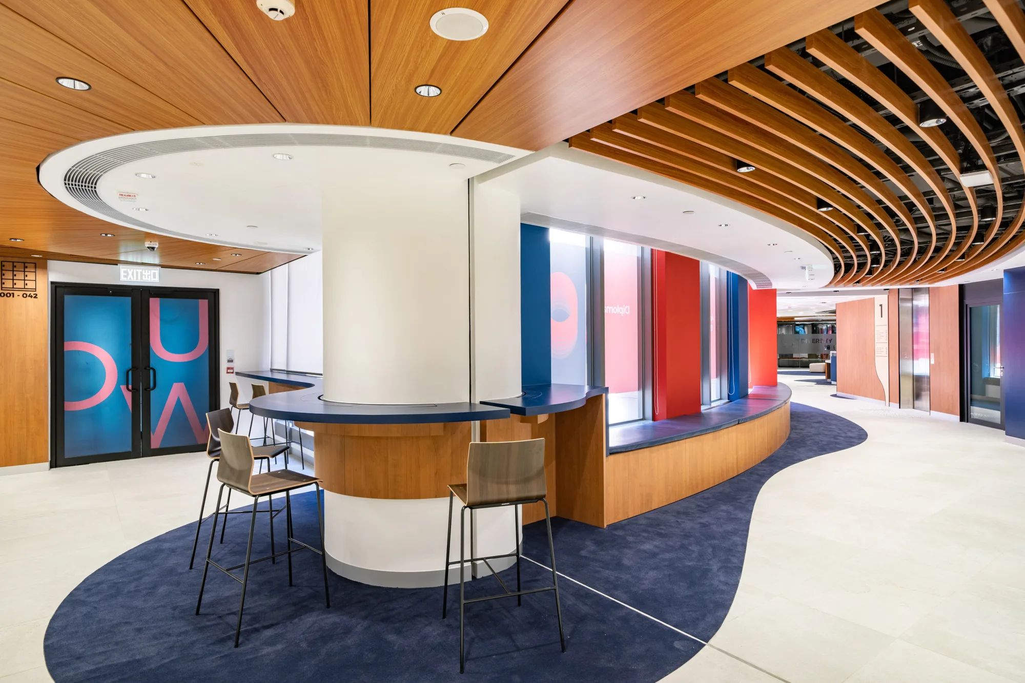 Brightly lit co-working space with full-length windows allowing natural light to filter in; features long table with high-top chairs and seating area along the window