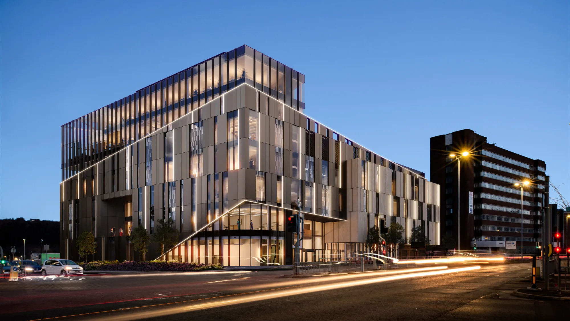 Exterior of the University of Huddersfield at dusk, showing internal lighting and car light trails in the foreground