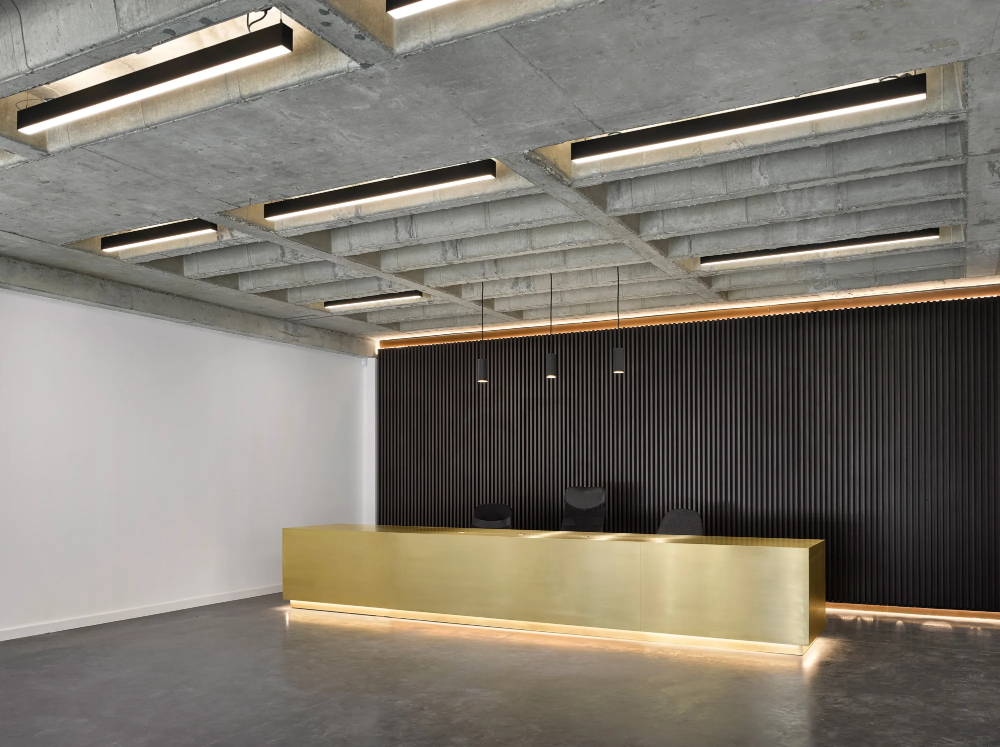 Interior of Wellington House, a modern office space with three chairs, a long wooden desk across and a dimly lit black feature wall behind