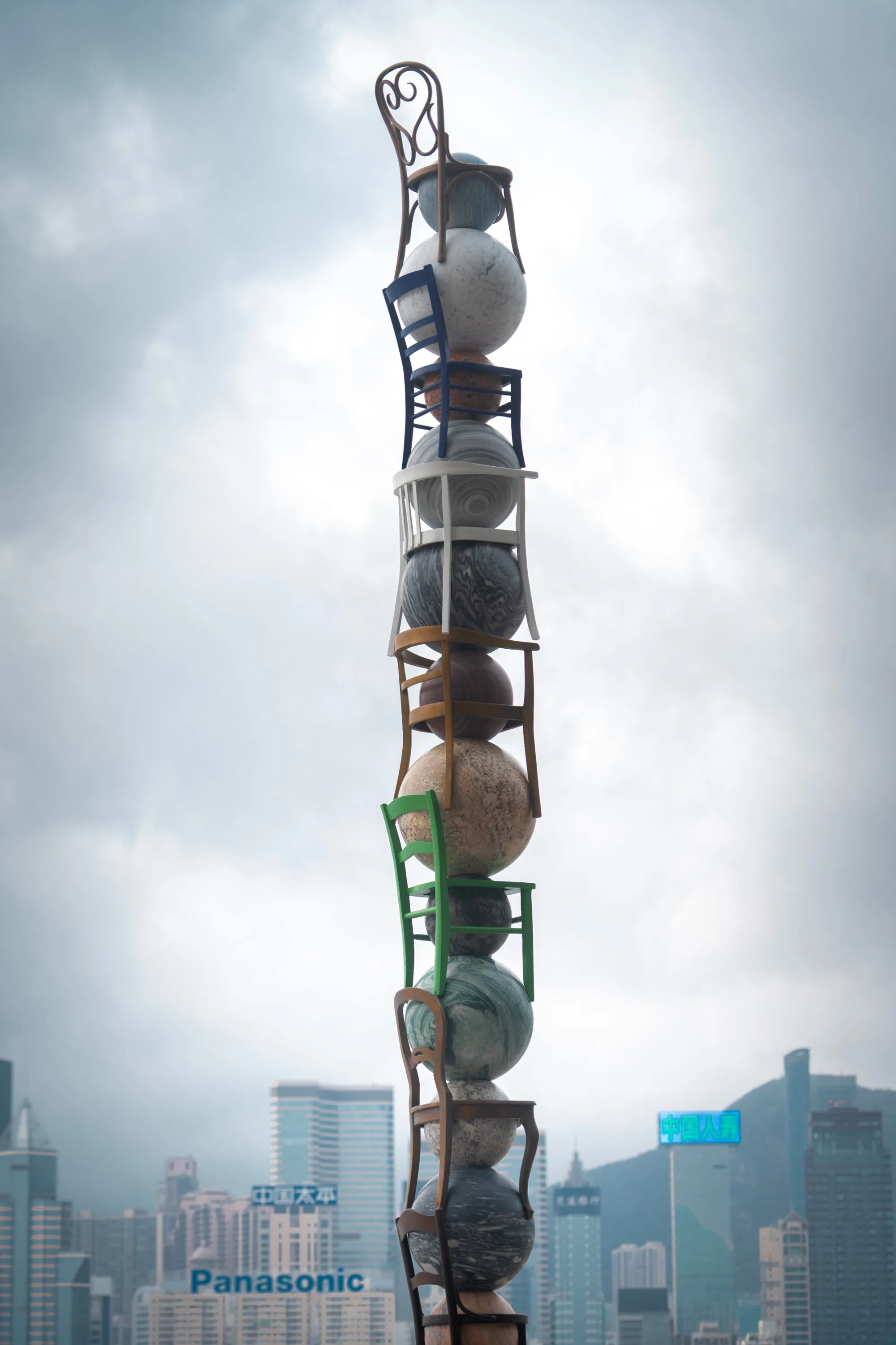 The artwork features seven marble spheres representing planets, suspended above a framework made of ordinary chairs