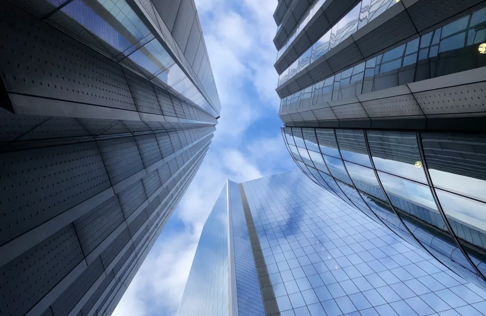 Looking up at glazed highrise buildings into a lightly clouded sky.