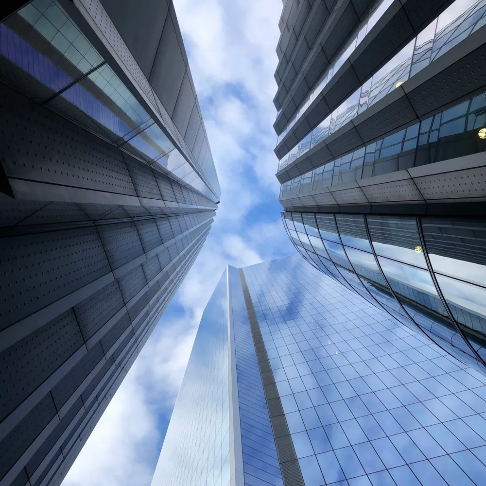 Looking up at glazed highrise buildings into a lightly clouded sky.
