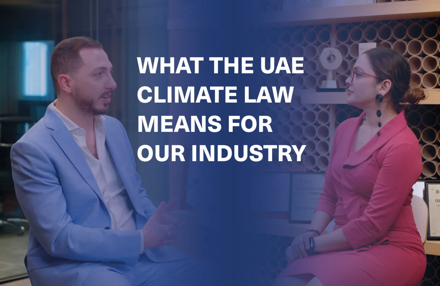 Two people seated across from each other in a professional setting; one in a light blue suit, the other in a red dress. Background shows circular-shelved wall and framed certificates. Text reads: “WHAT THE UAE CLIMATE LAW MEANS FOR OUR INDUSTRY”.