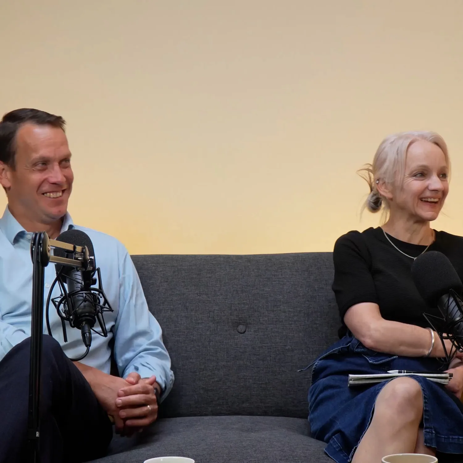 Robin and anna sat on a sofa with podcast mics