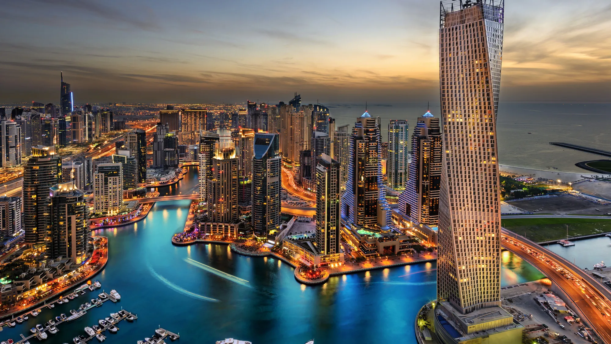 Boats in Dubai marina with orange lit buildings against a dusk sky