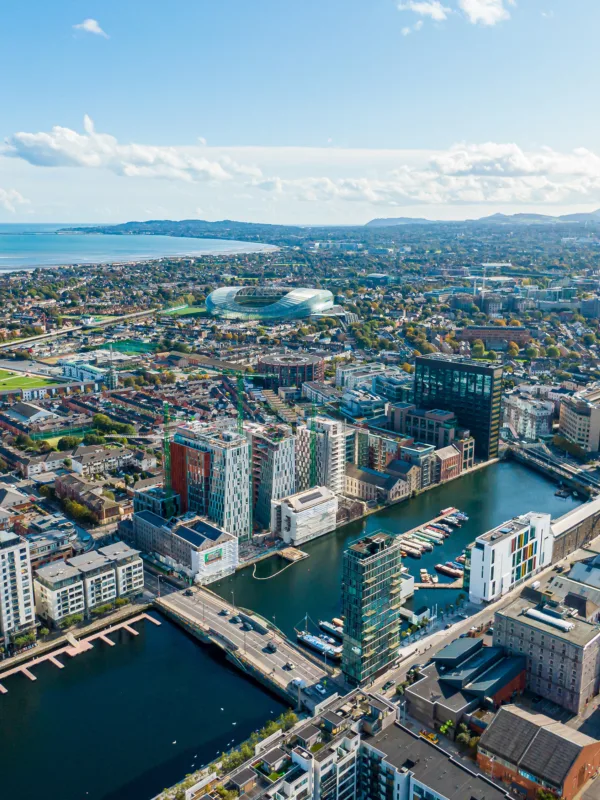 Aerial view of a cityscape featuring modern and traditional buildings, a central body of water, high-rise structures, residential areas, hills, and a coastline in the background.