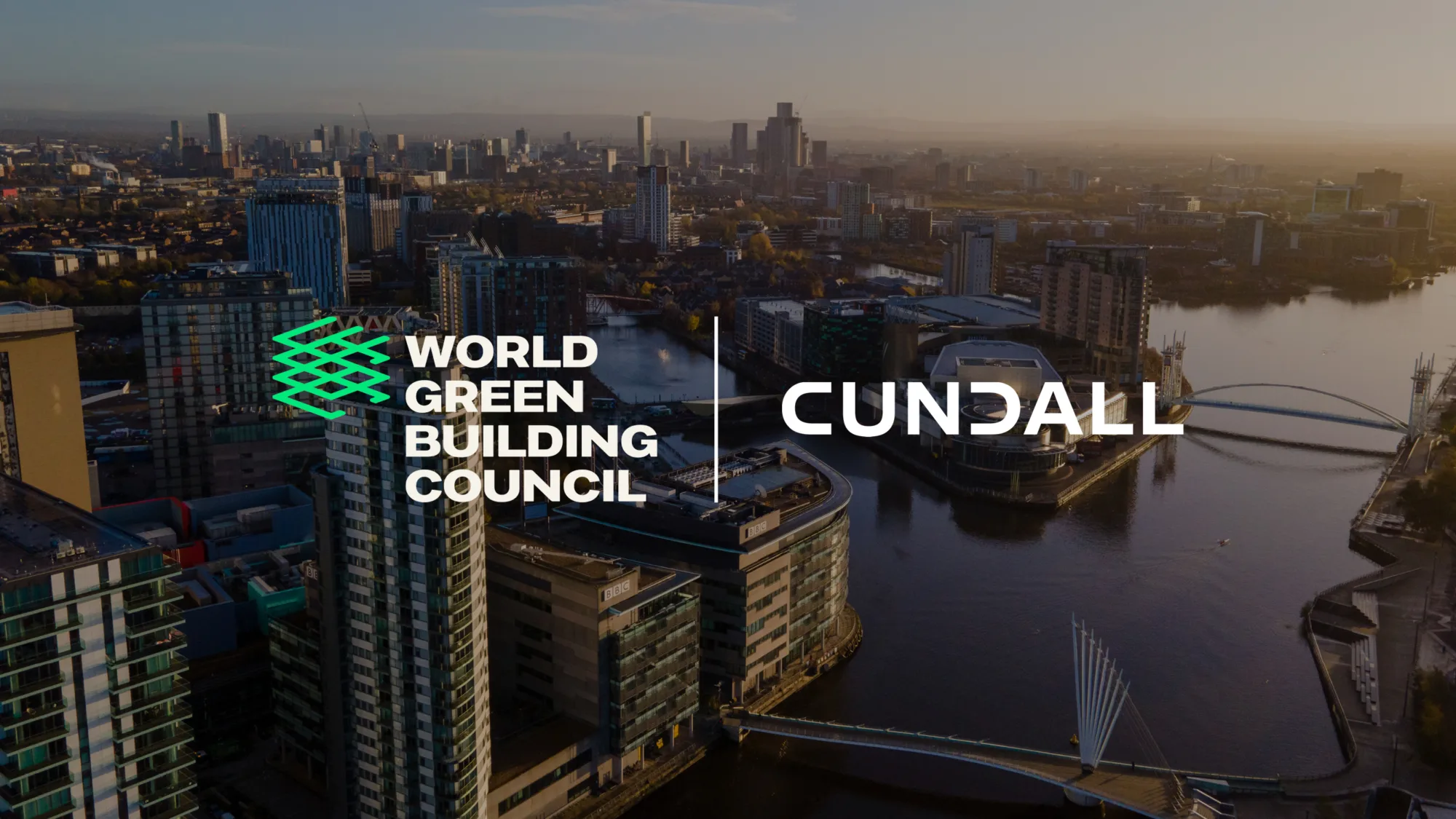 Aerial view of a modern cityscape with high-rise buildings along a river, bridges crossing the water, and urban streets. The image includes two logos: “World Green Building Council” in white and green on the left and “Cundall” in white on the right, positioned over the city background.